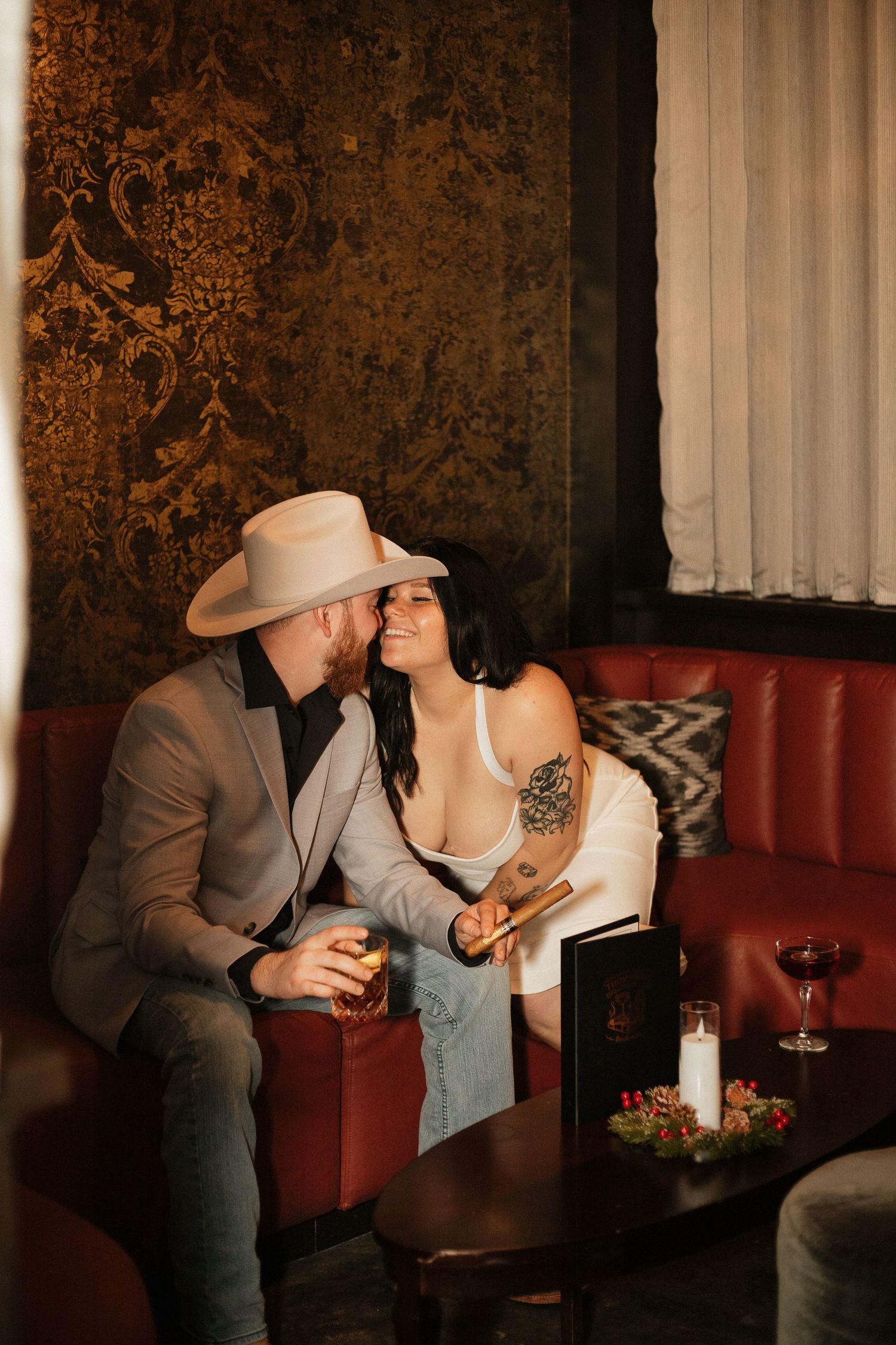 Romantic couple sharing intimate moments at a dimly lit restaurant booth with wine glasses and candlelight.