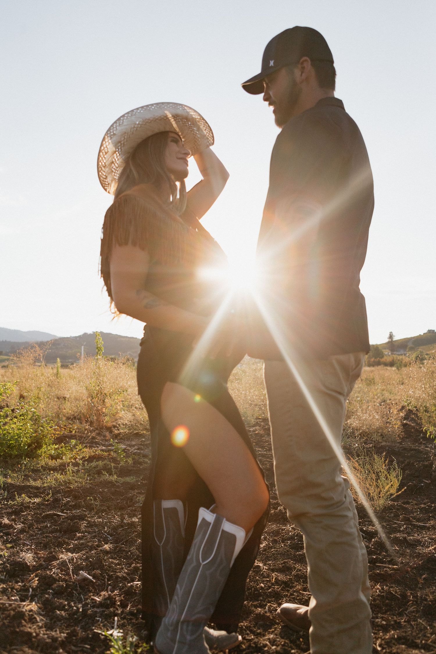 A maternity couple embraces in silhouette against golden sunlight in a rustic outdoor setting during sunset in Caddo Mills, Texas