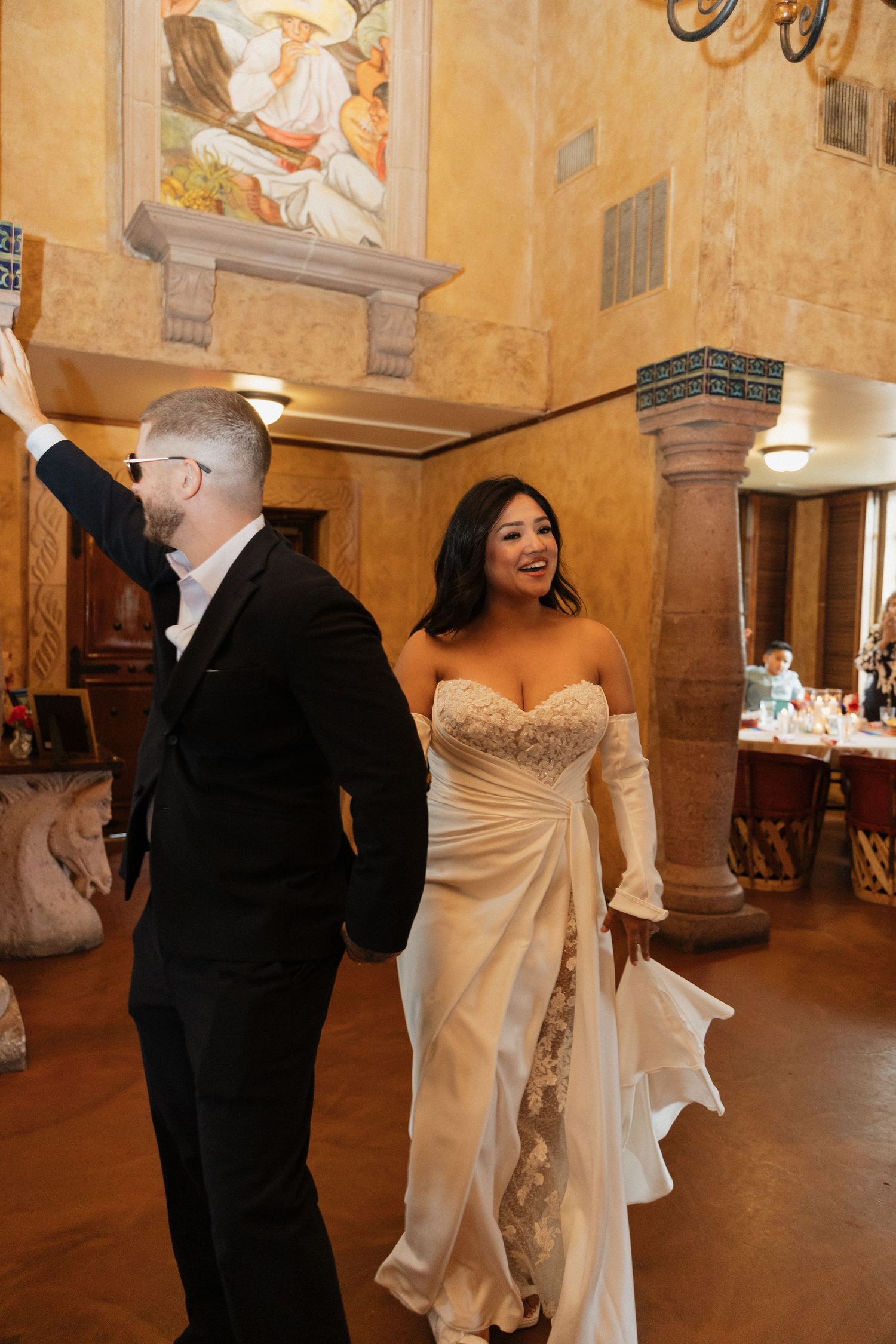Bride in white lace gown and groom in black suit share first dance in elegant venue with murals.