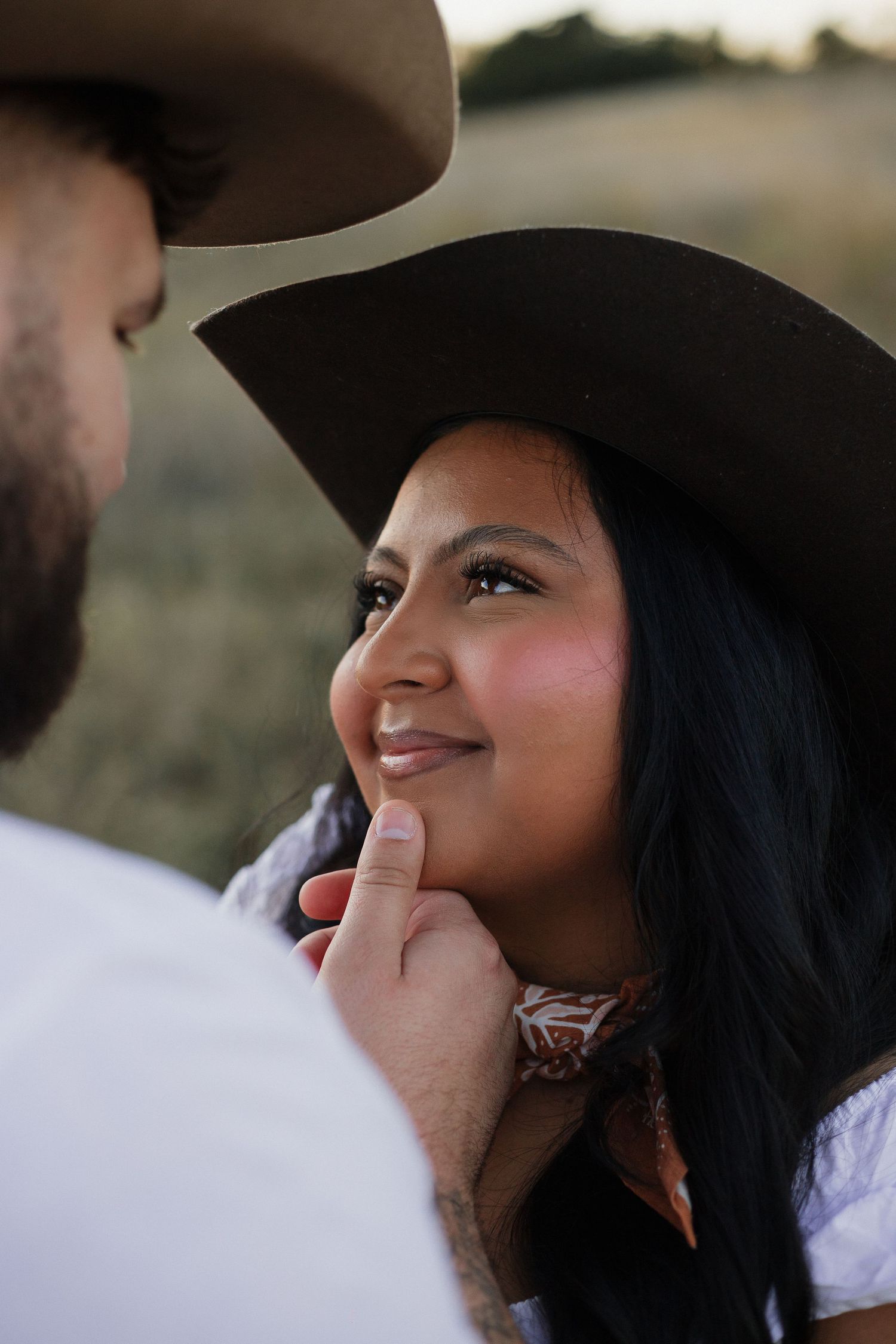 Close-up of tender moment between couple wearing western hats in outdoor setting.