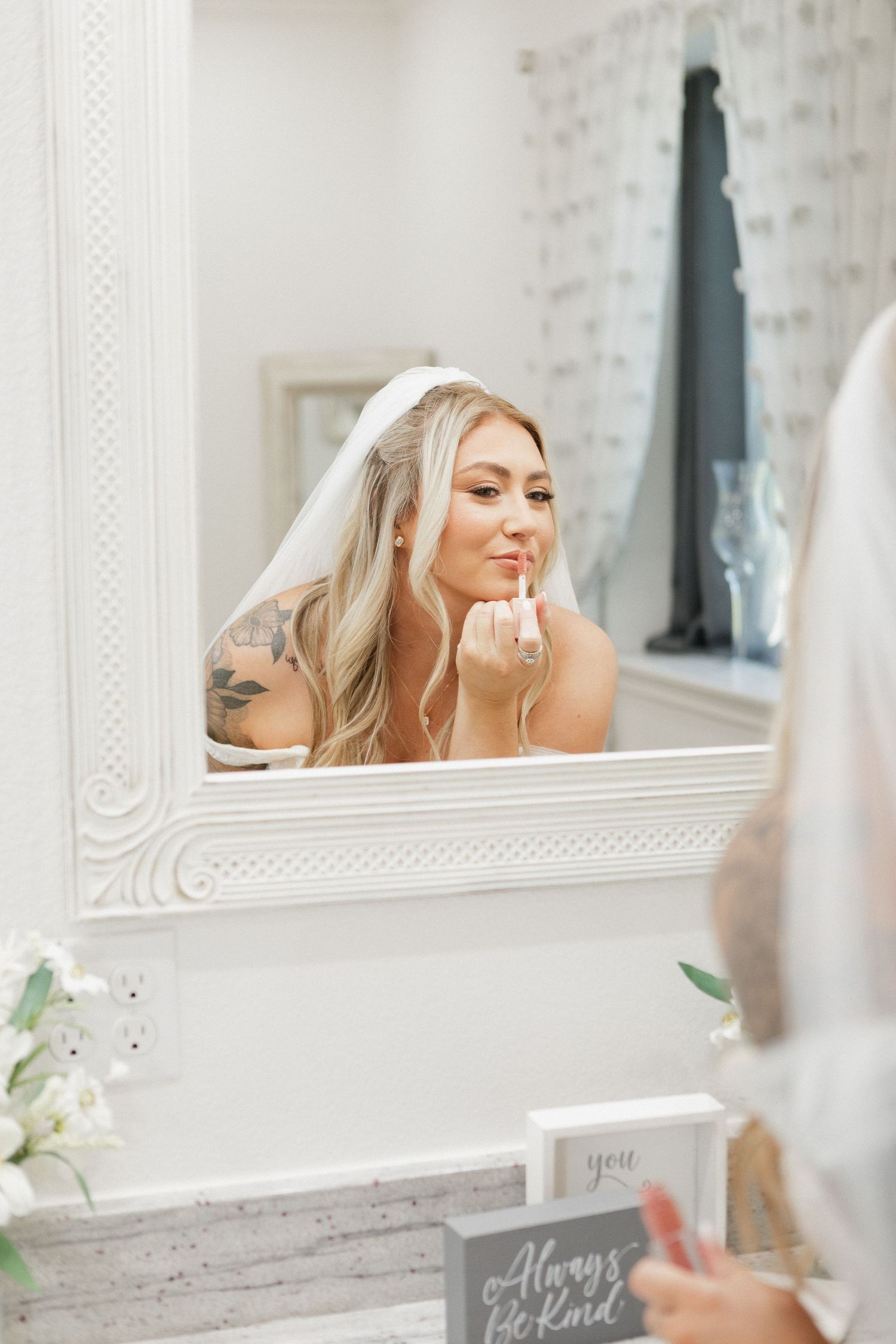 Bride getting ready in front of an ornate white mirror on her wedding day.