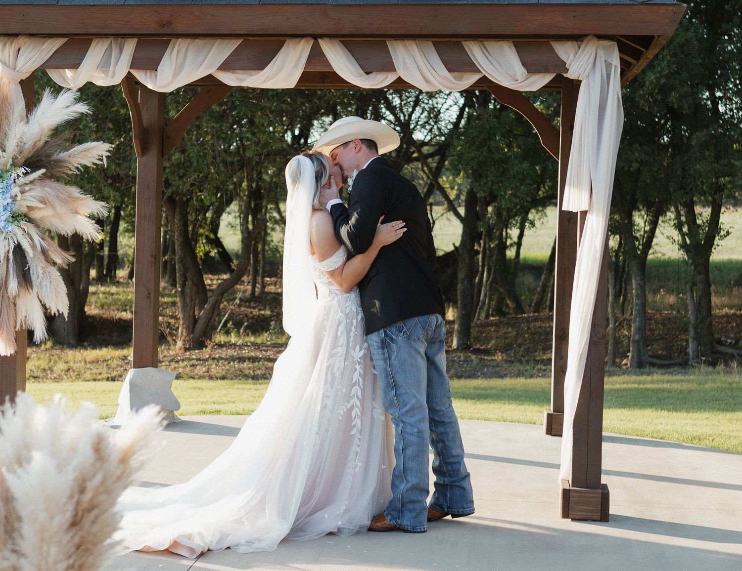 A couple shares a tender moment under a gazebo during their outdoor wedding ceremony.