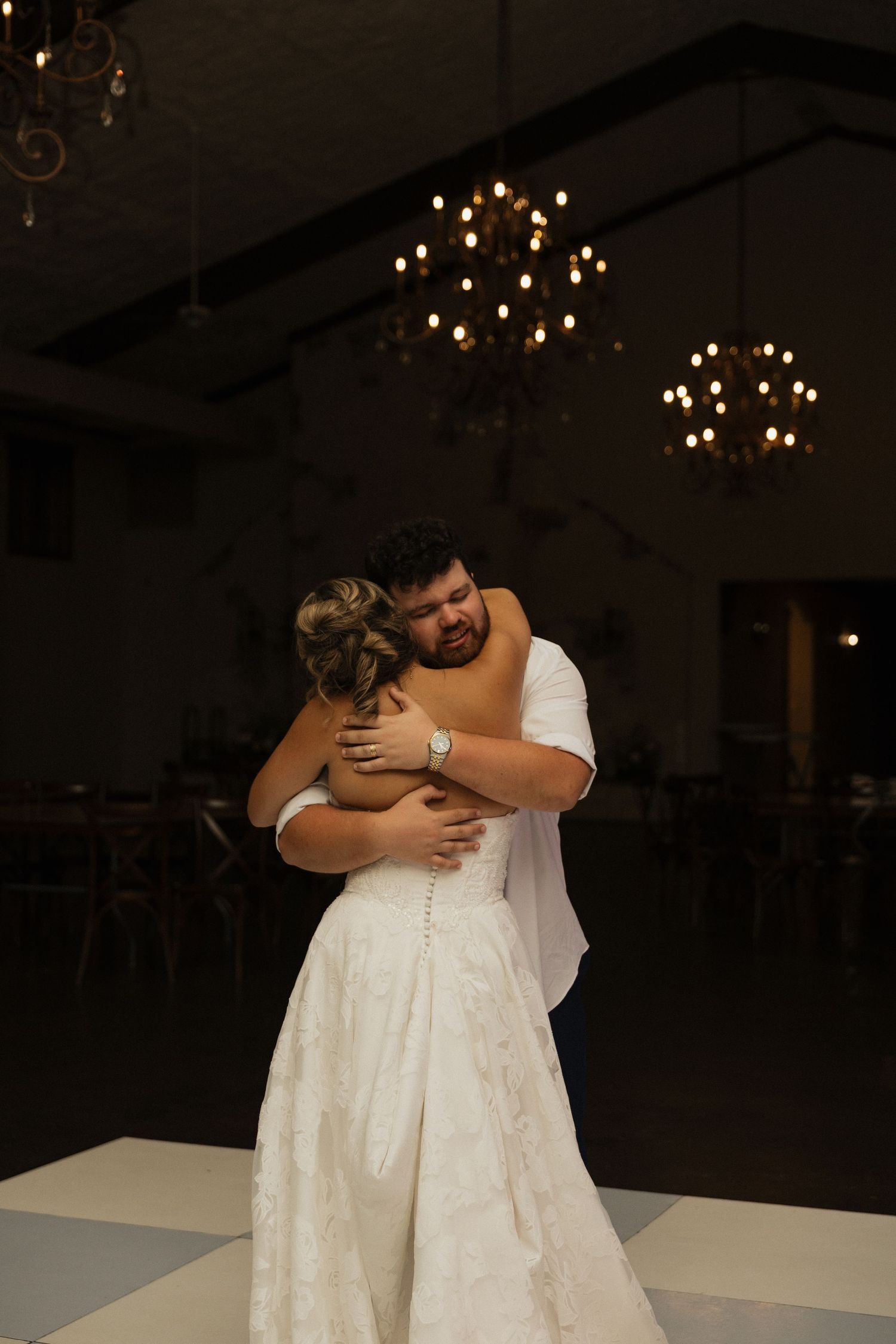 Bride and groom share an emotional first dance embrace under warm chandelier lighting at their wedding reception.