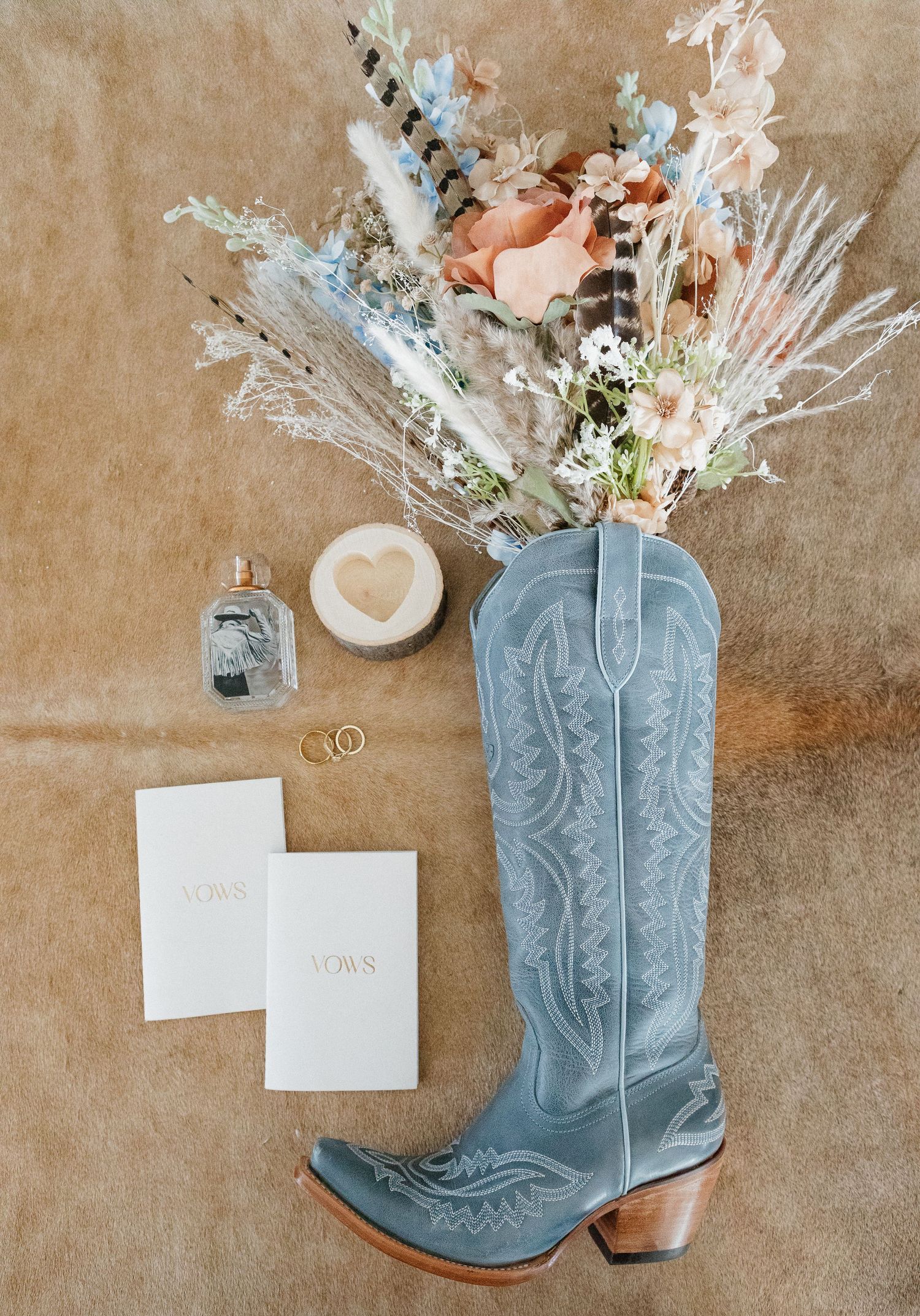 A pair of light blue cowboy boots filled with dried flowers and wedding stationery arranged in a rustic setting.