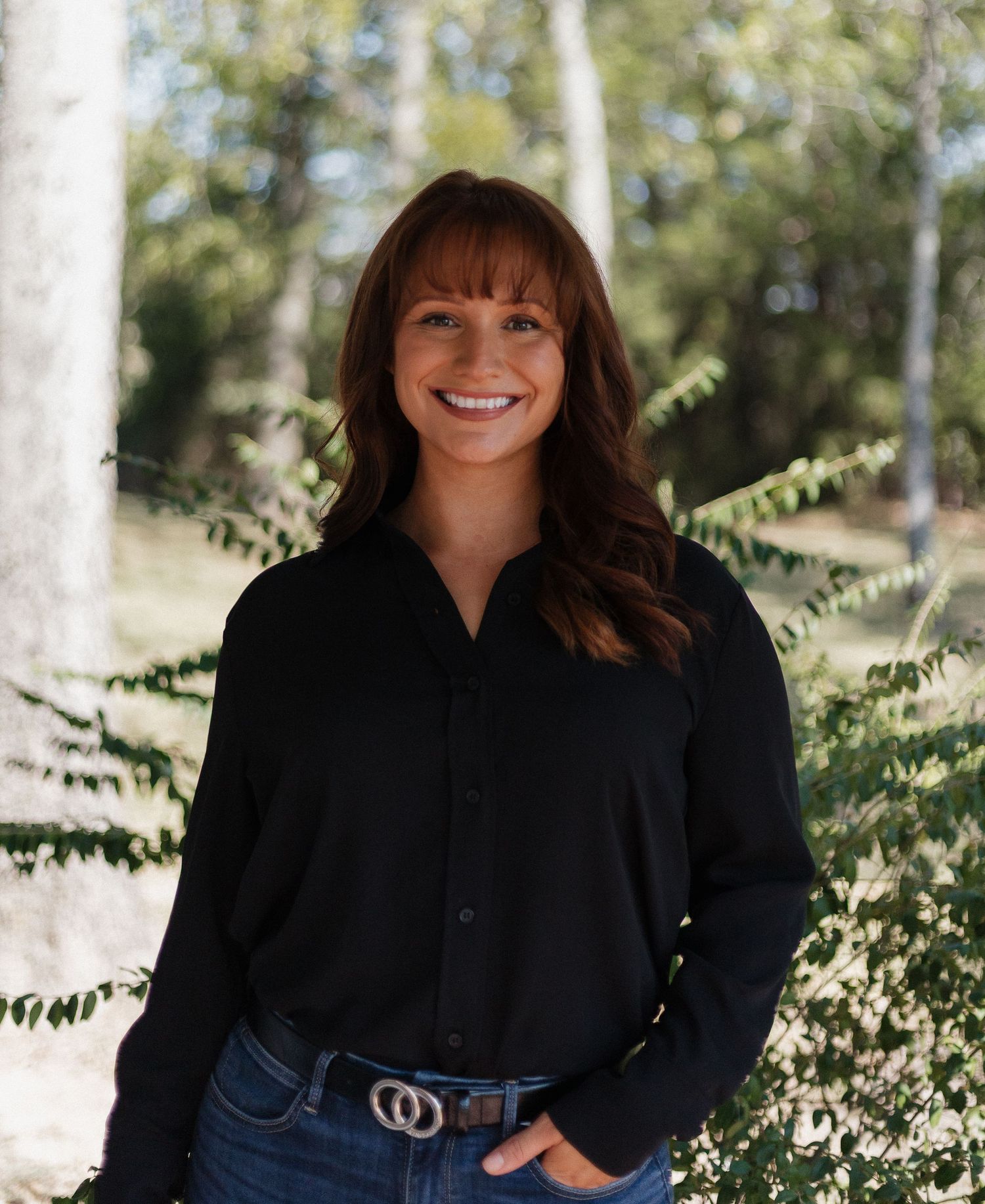 A person wearing a black jacket poses outdoors against a natural backdrop.