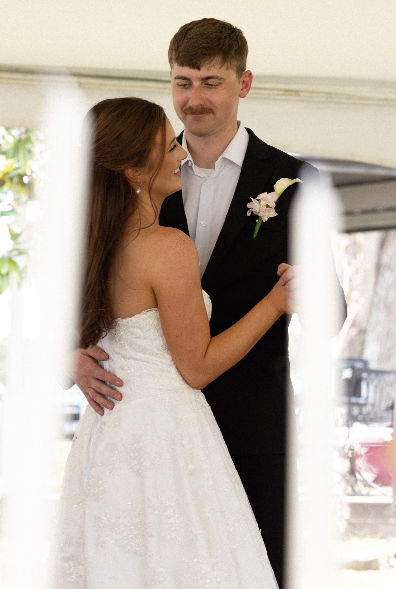 A couple shares their first dance at a wedding reception under a white tent, with the bride in a strapless gown.
