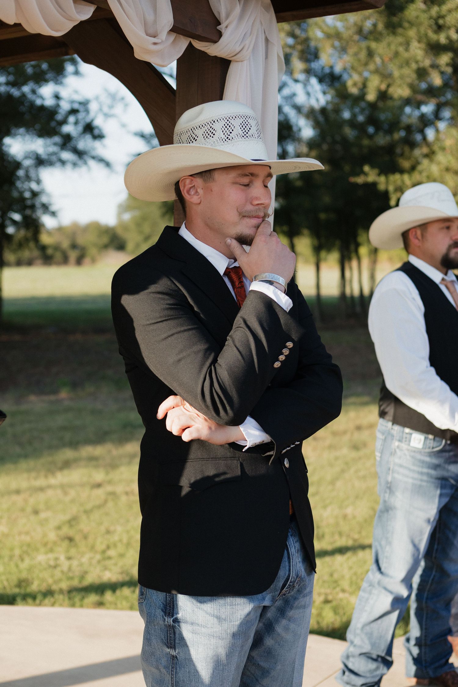 Men in cowboy hats and formal wear embracing during a wedding celebration.