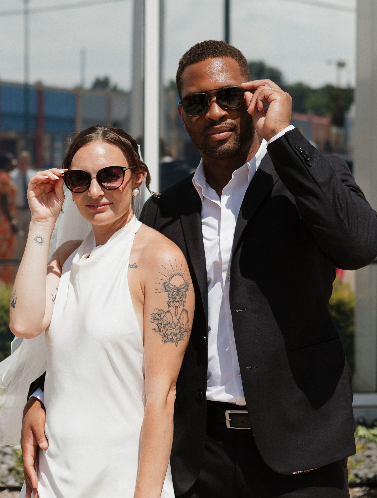 A group of people wearing sunglasses and formal attire pose together outdoors on a sunny day.