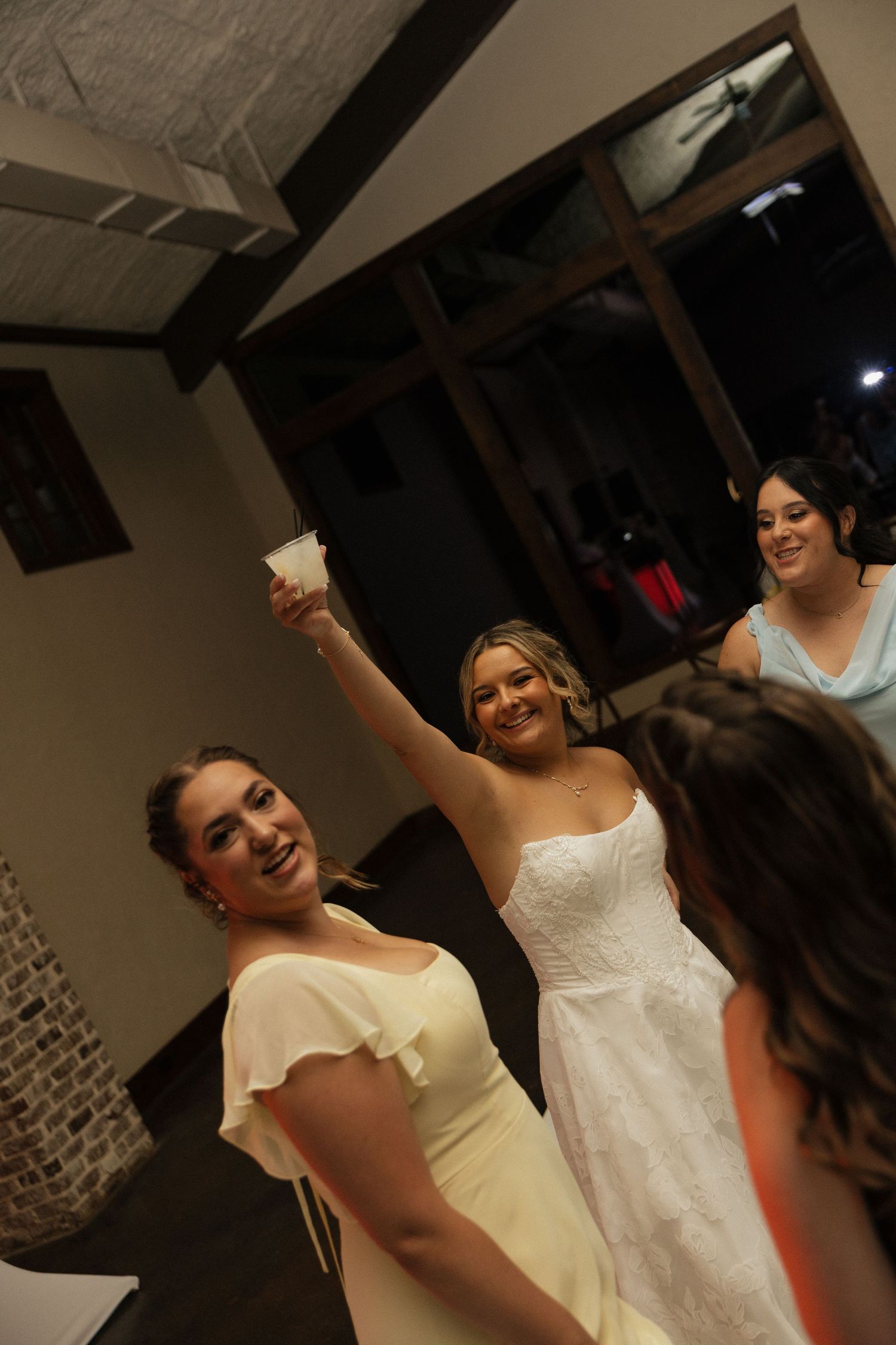 Bride in white gown raises a toast with bridesmaids in yellow dresses at an elegant wedding reception.