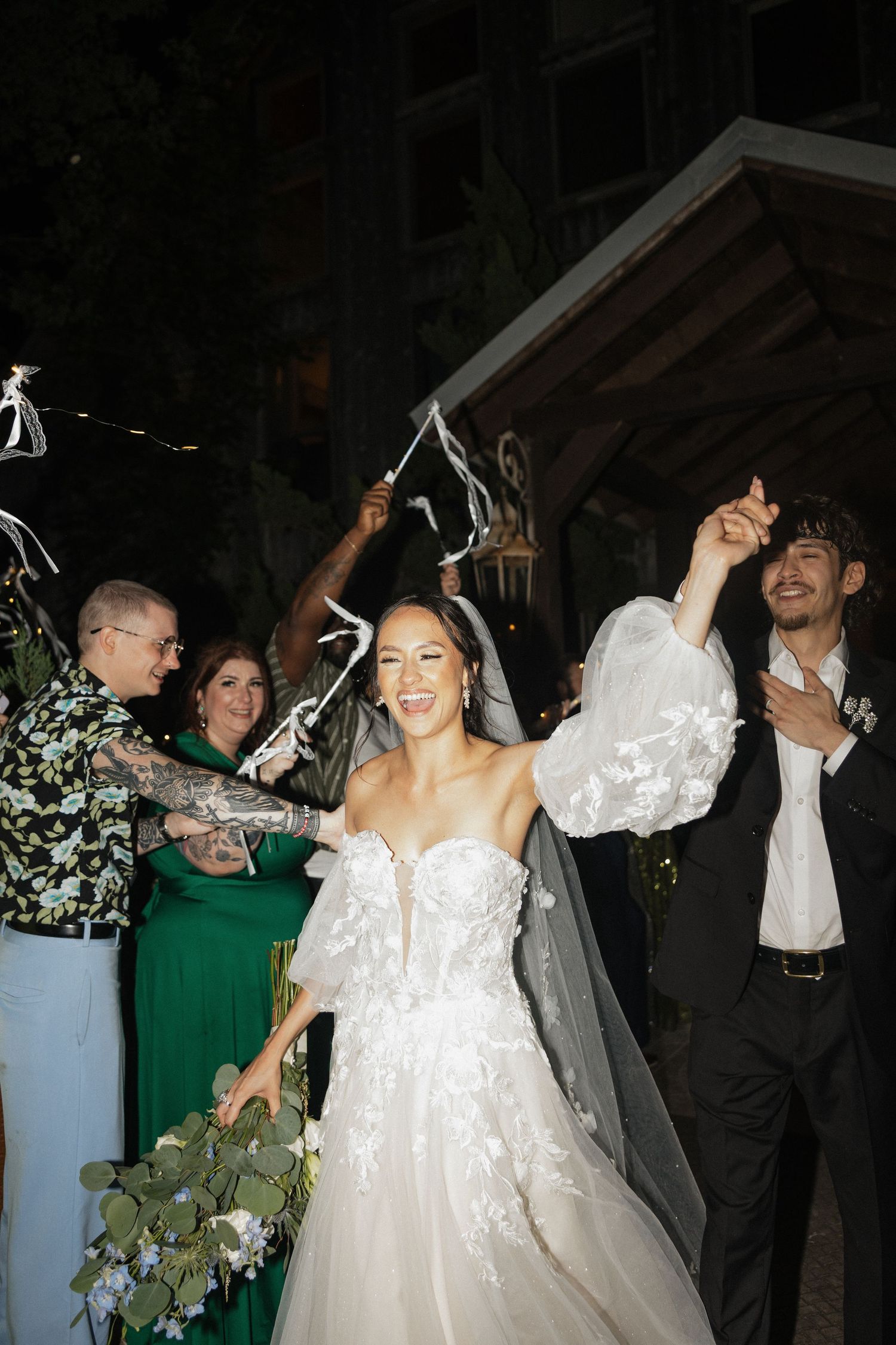 Bride in white floral gown and veil laughs joyfully during wedding sendoff with guest waving ribbons. Caddo Mills Texas wedding photographer