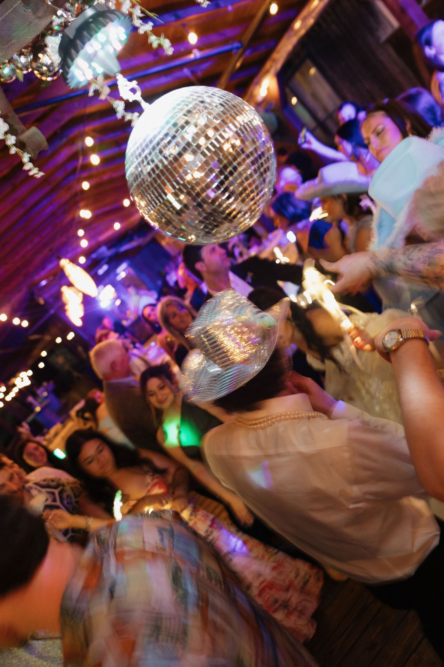 Lively dance party with a sparkling disco ball hanging above energetic crowd in a warmly lit venue.