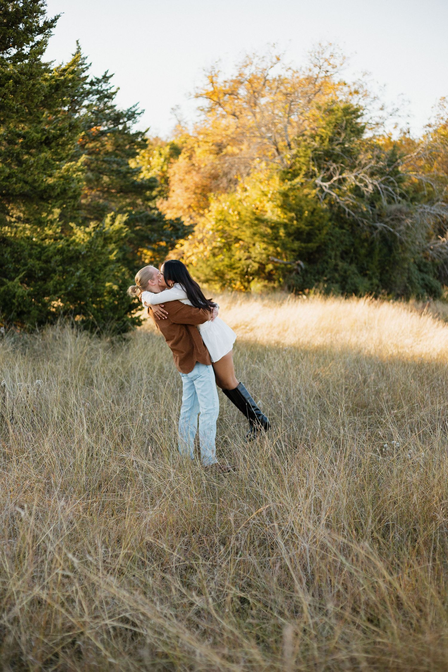 Joyful embrace in a golden field with autumn trees in the background.