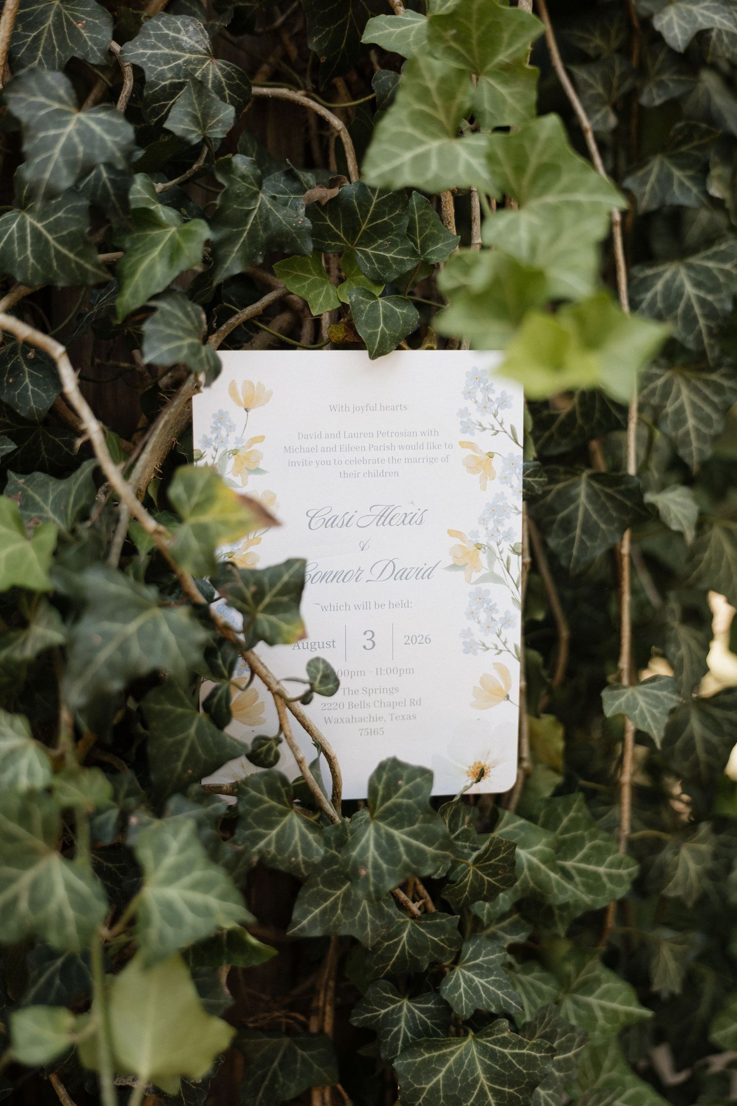 Elegant wedding invitation with floral details displayed against lush green ivy backdrop.