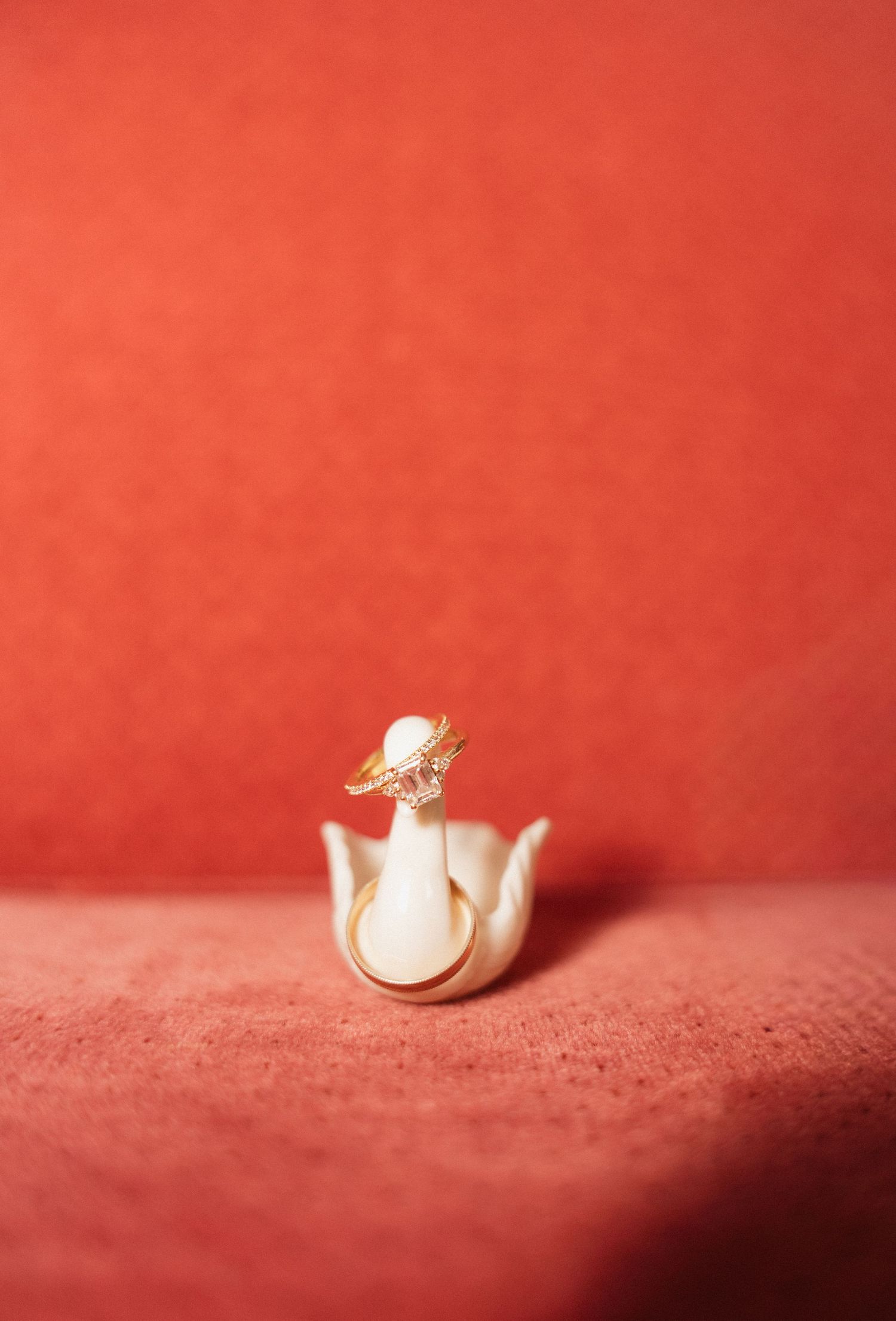 Gold diamond ring displayed in a white tulip ring holder against a red background.