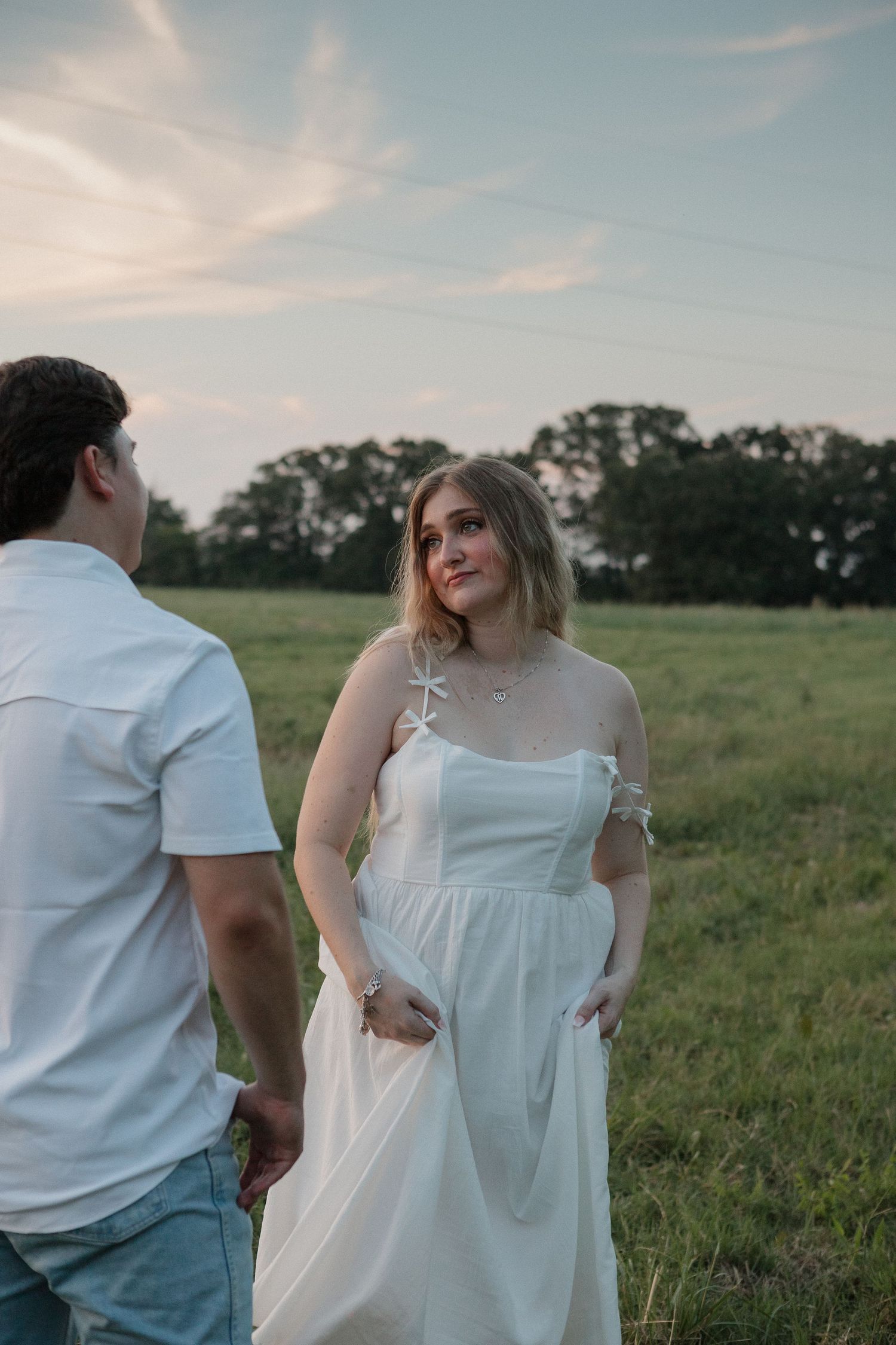 A couple in white clothing stands together in a green meadow at sunset, creating a romantic silhouette against nature Gun Barrel City, Texas