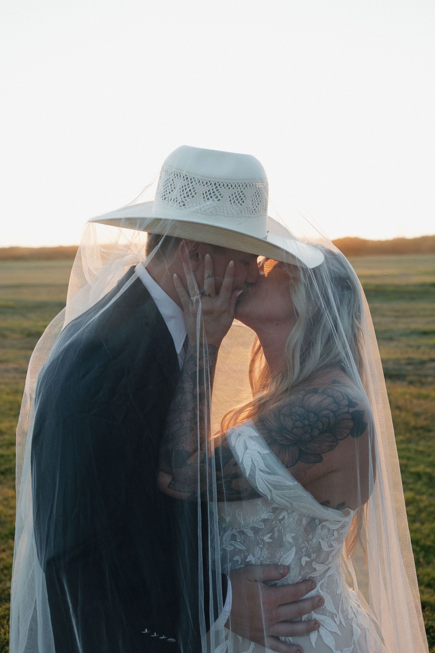 Romantic sunset portrait of couple under bridal veil in country setting.
