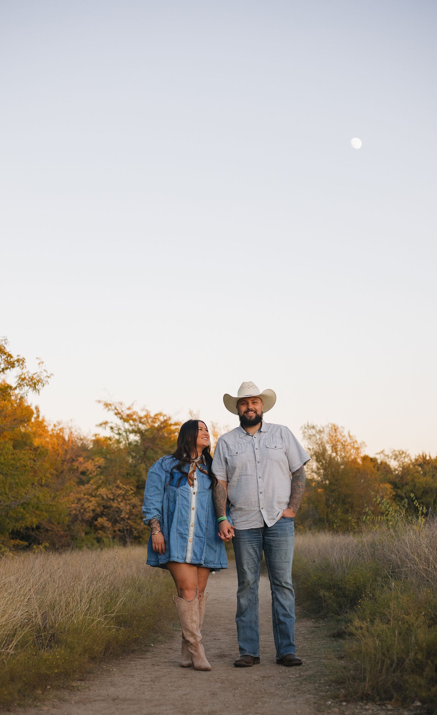 Couple walking together in a field at sunset wearing cowboy boots and casual western attire.