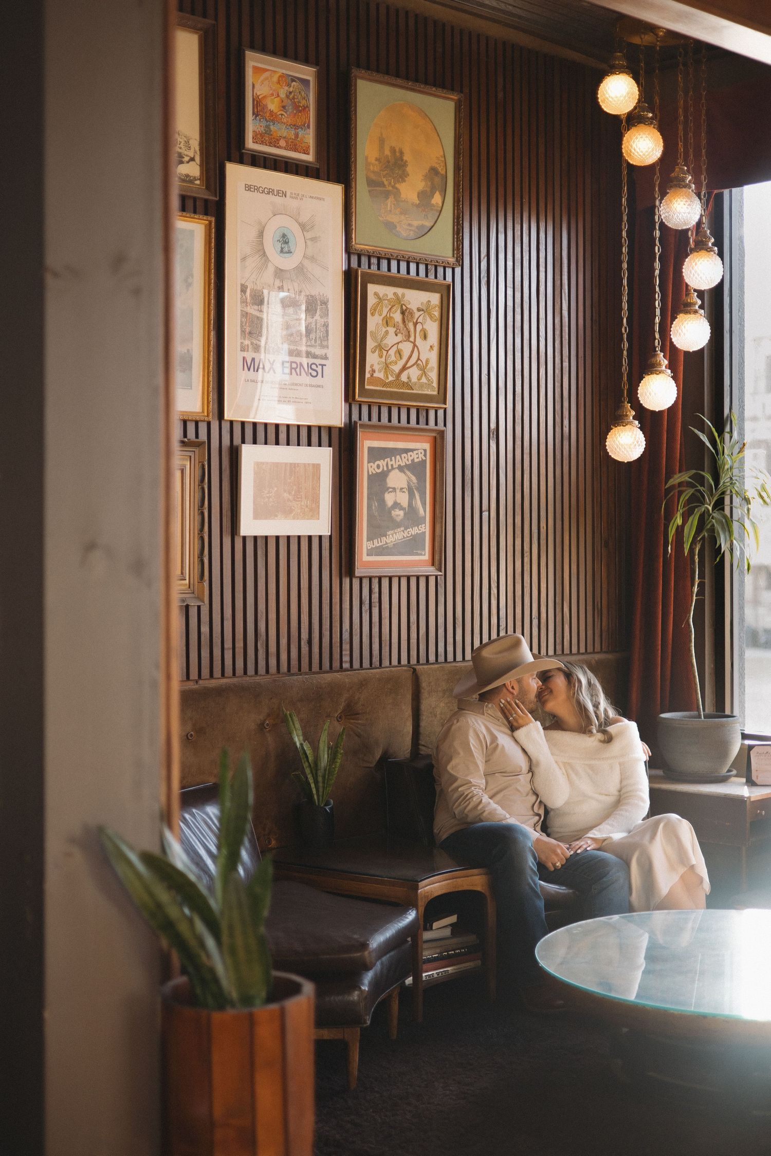 Couple sharing a romantic kiss on a cozy cafe booth, surrounded by vintage wall art and warm Edison bulb lighting.