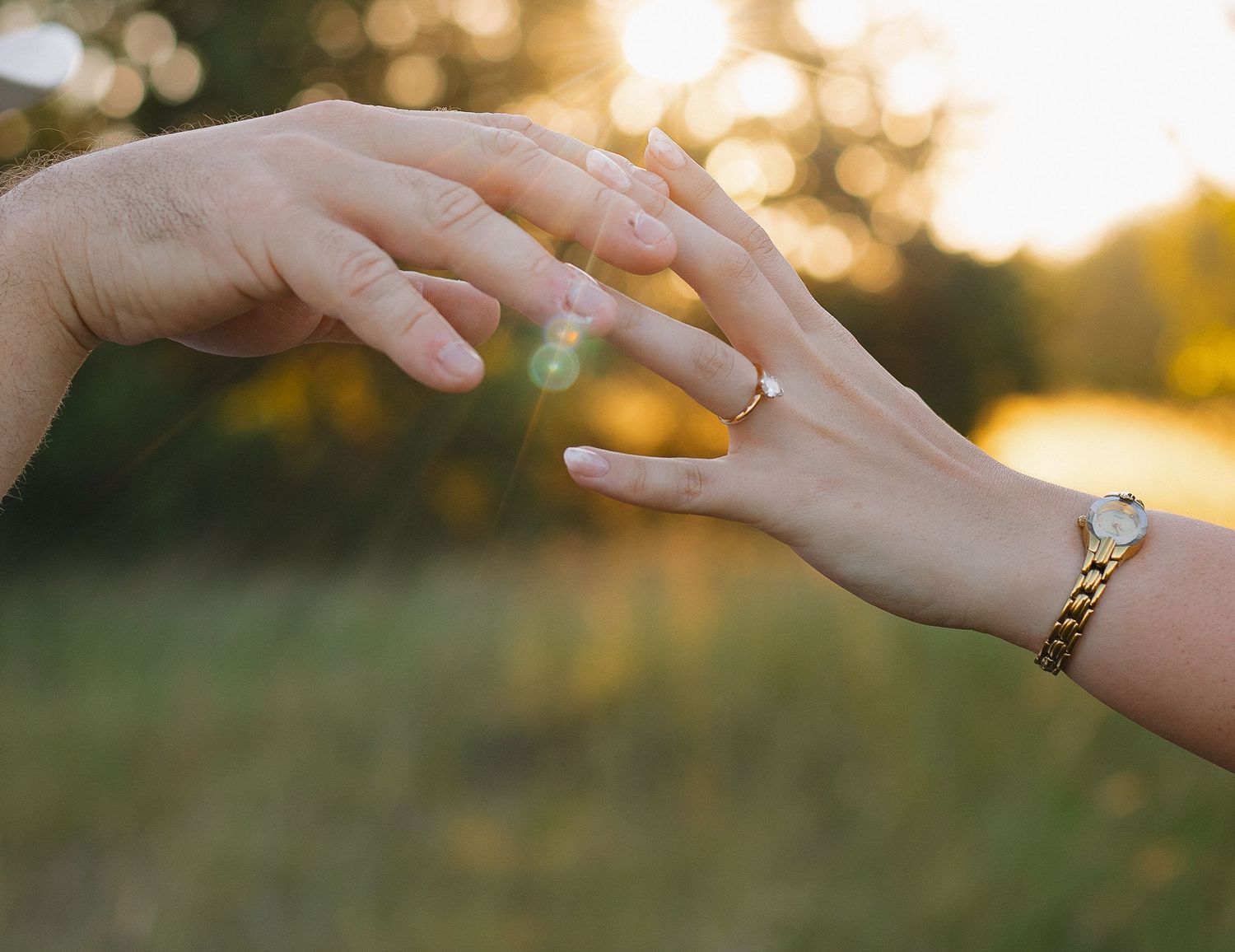 Close-up of hands with engagement ring in golden sunset light.