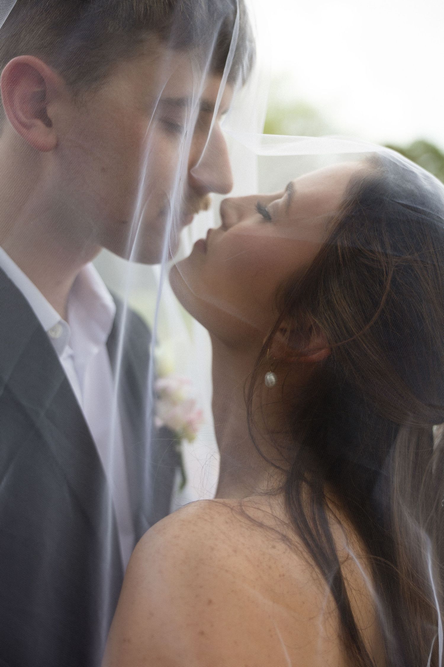 A romantic wedding moment shows a couple sharing a tender kiss in formal attire outdoors.
