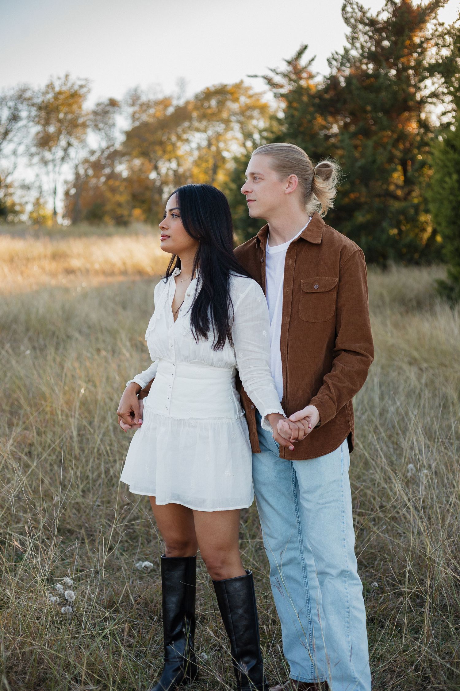 Couple in contrasting outfits standing together in an autumn field at sunset.