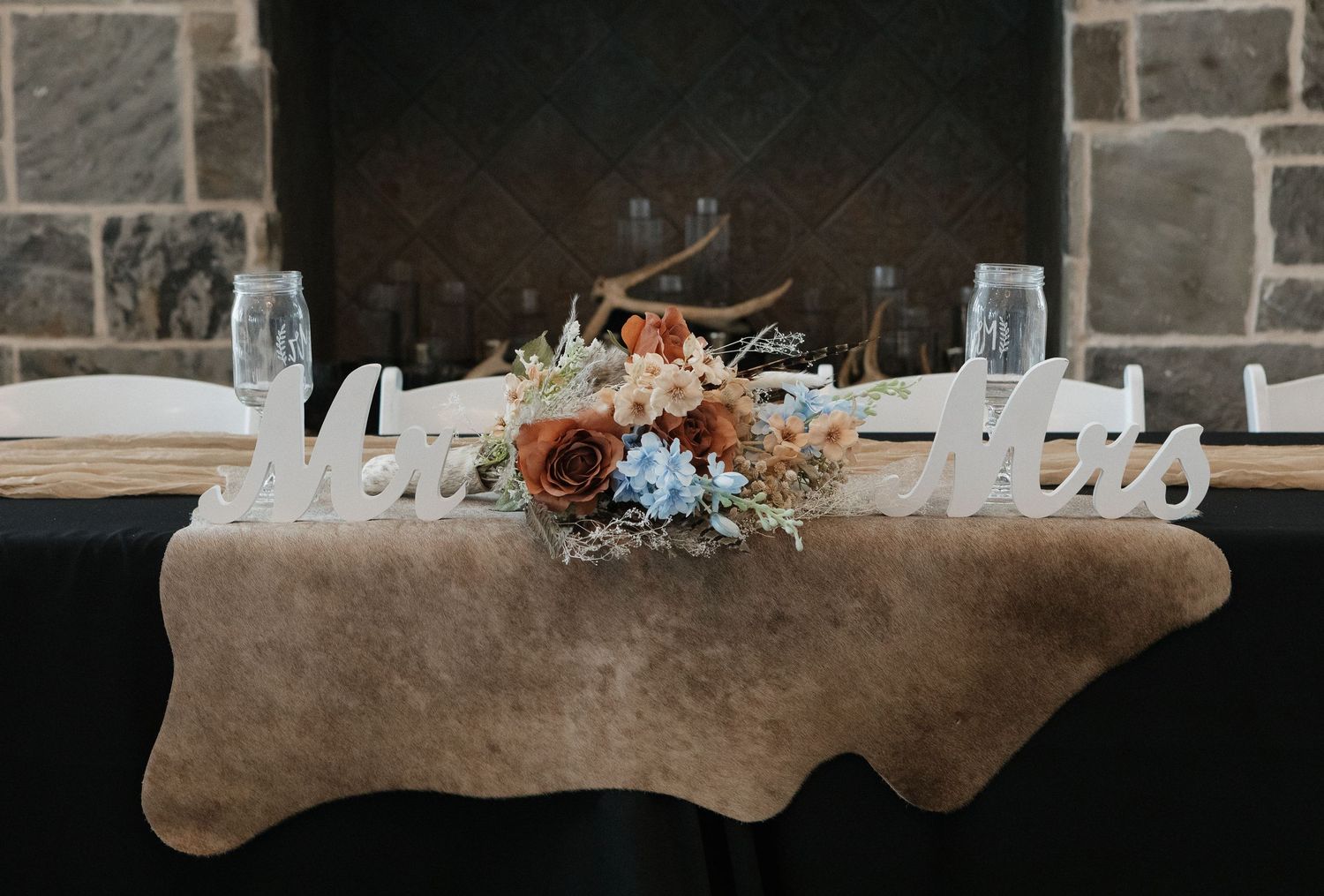 A rustic stone wall backdrop with elegant floral arrangements displayed on beige upholstered benches.
