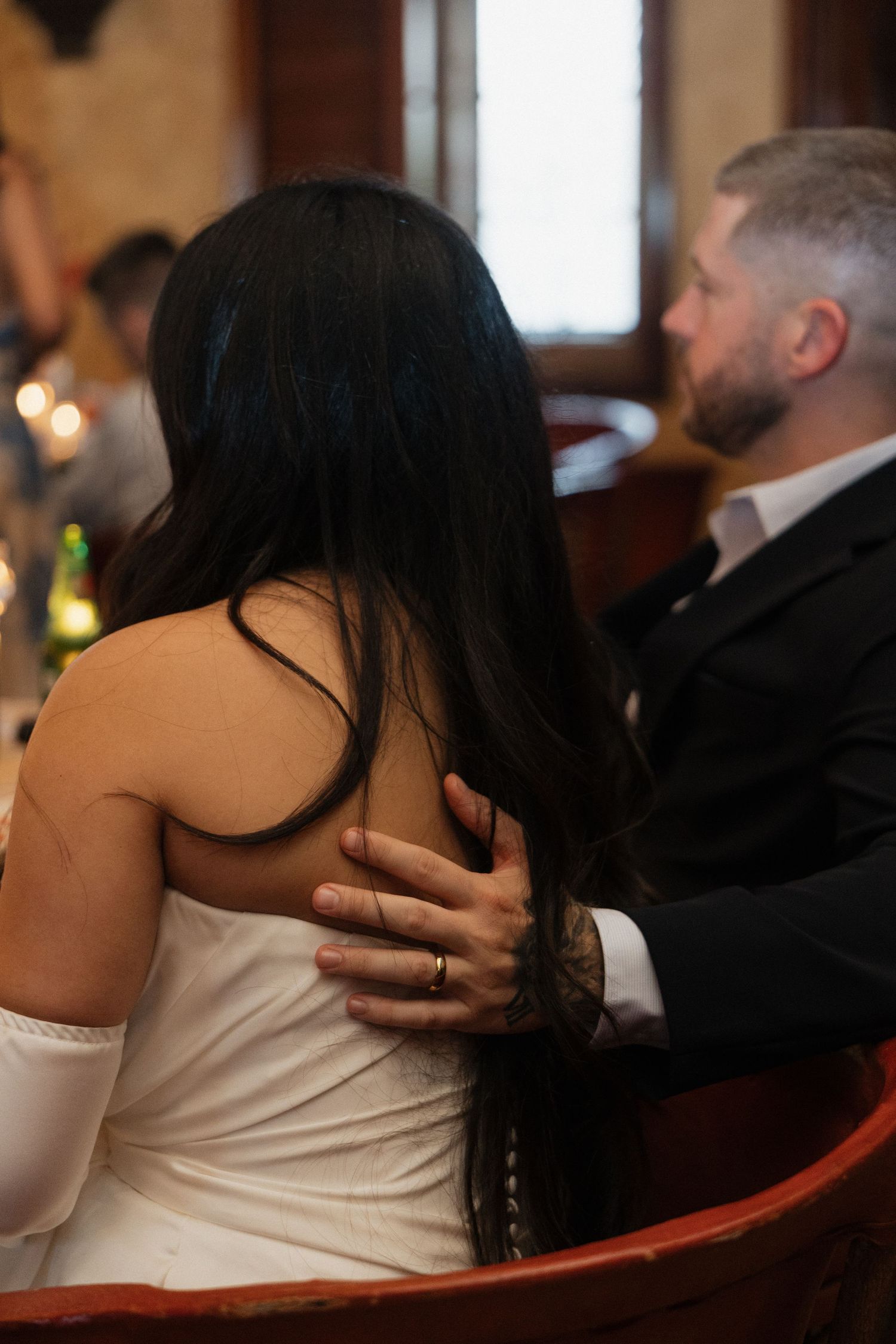 Groom tenderly embraces bride with wedding ring visible at reception dinner.