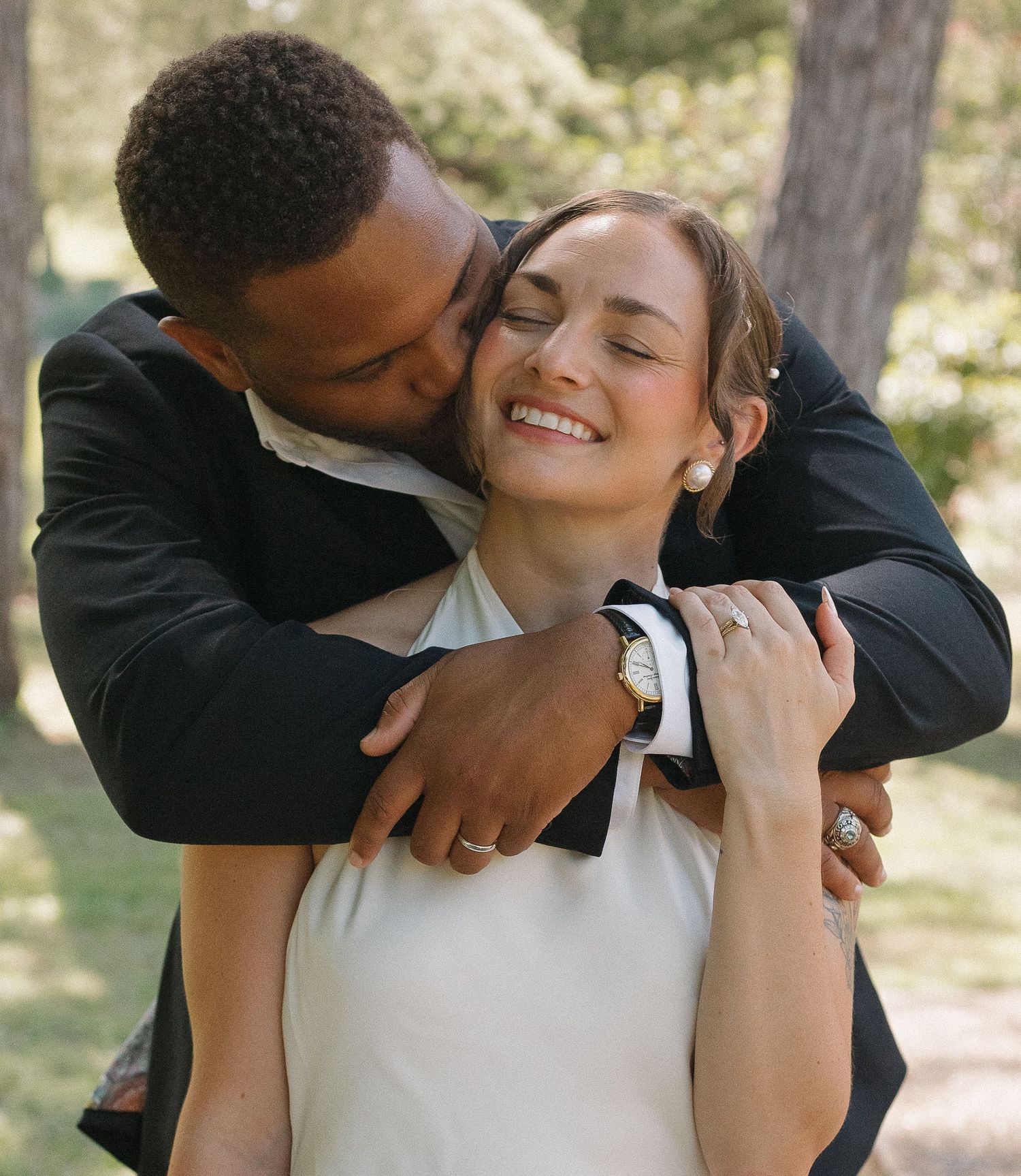 A couple shares an intimate embrace outdoors in a natural setting with trees in the background.