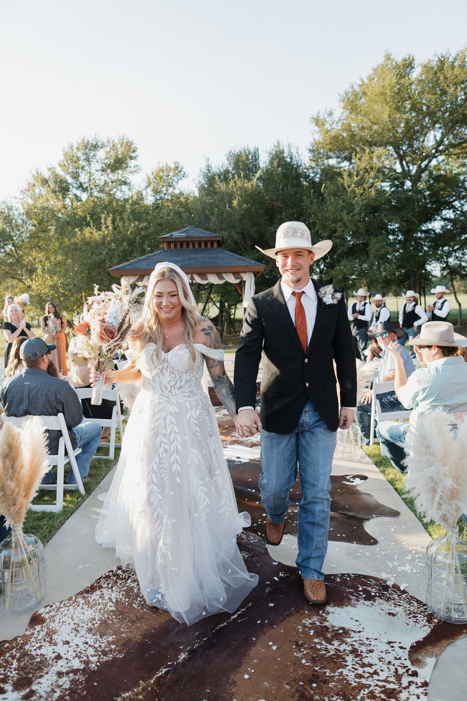 Wedding couple walking together outdoors with white flower petals scattered on the ground.