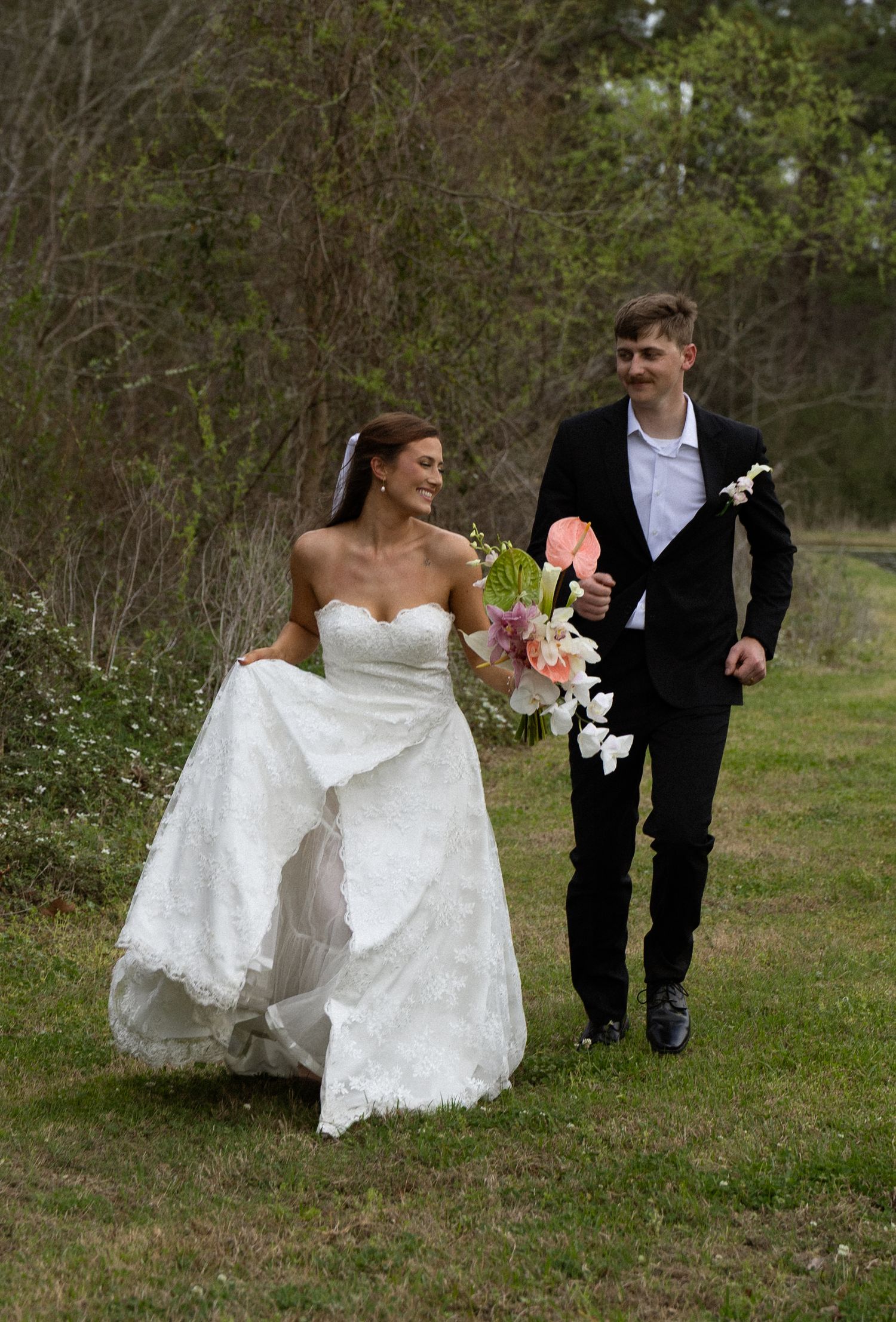 A couple in wedding attire walks together across a grassy outdoor area on their special day.
