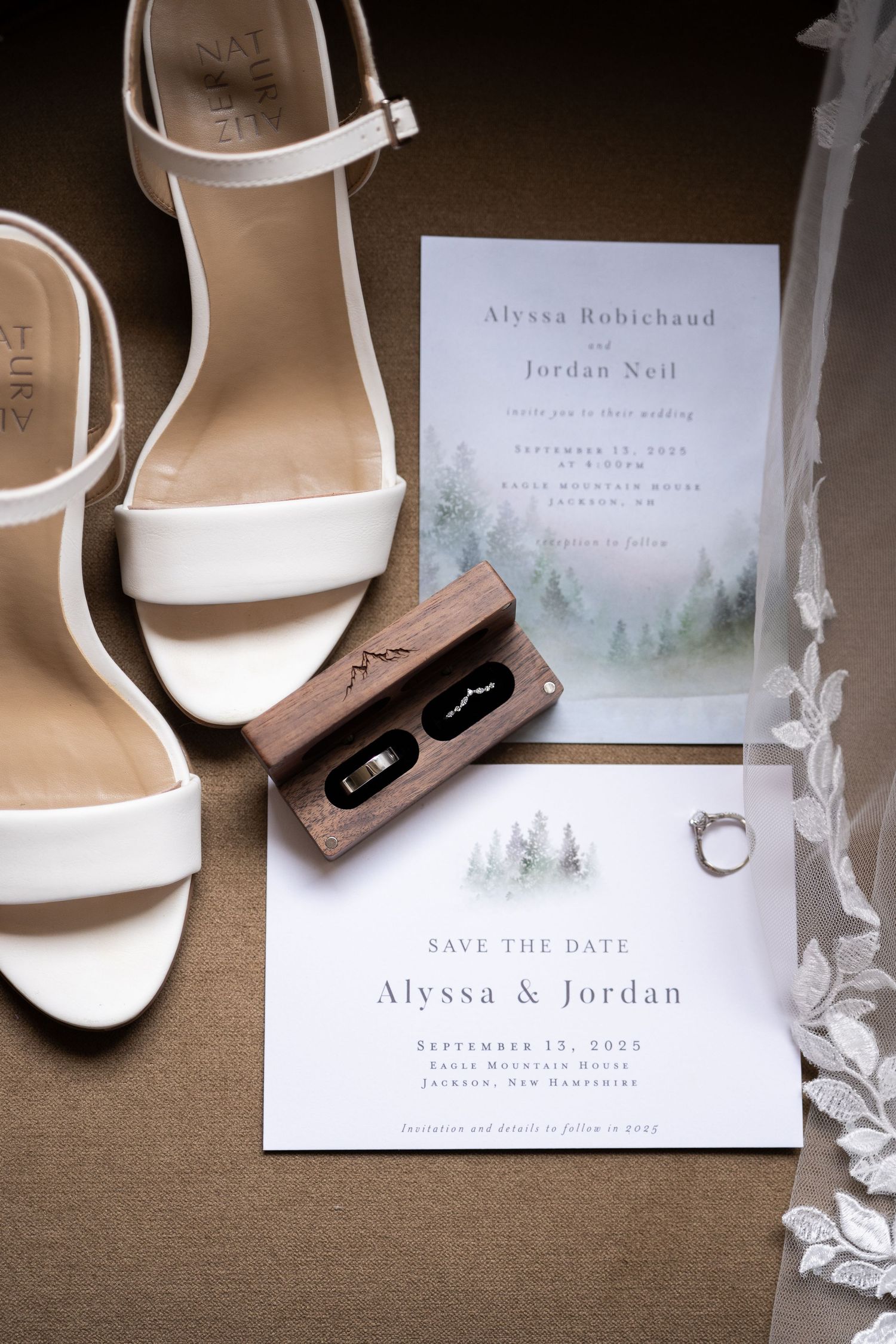 Wedding flat lay featuring white heels, wooden ring box, engagement ring, and elegant forest-themed invitations.