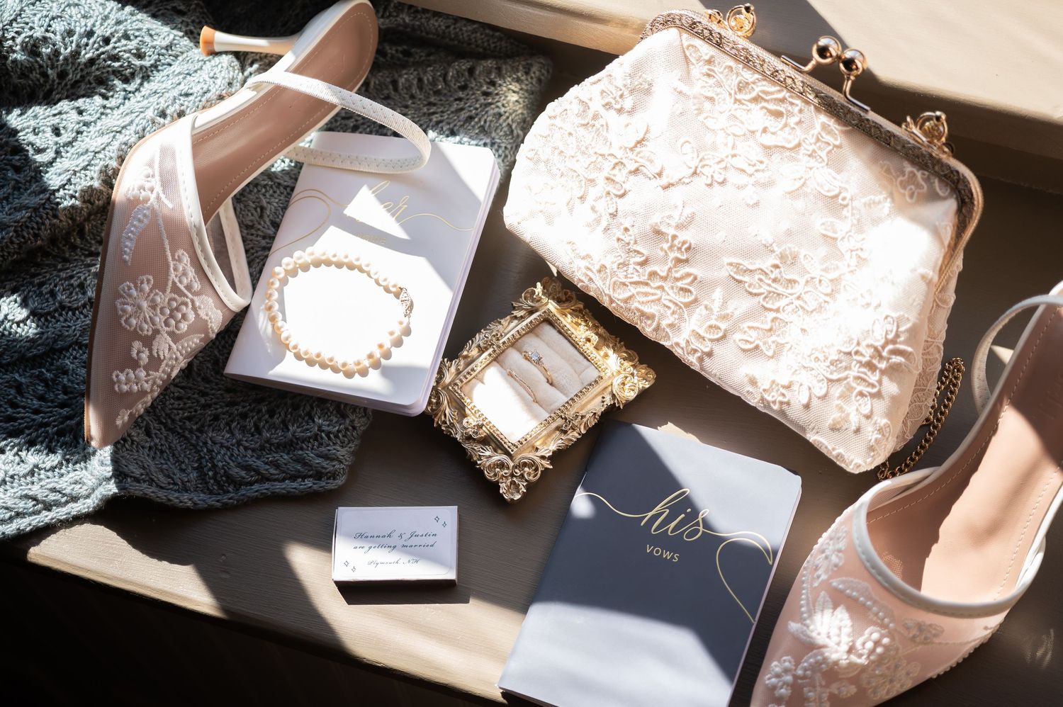 Flat lay of bridal accessories including lace heels, pearl bracelet, clutch, and watch on a table.