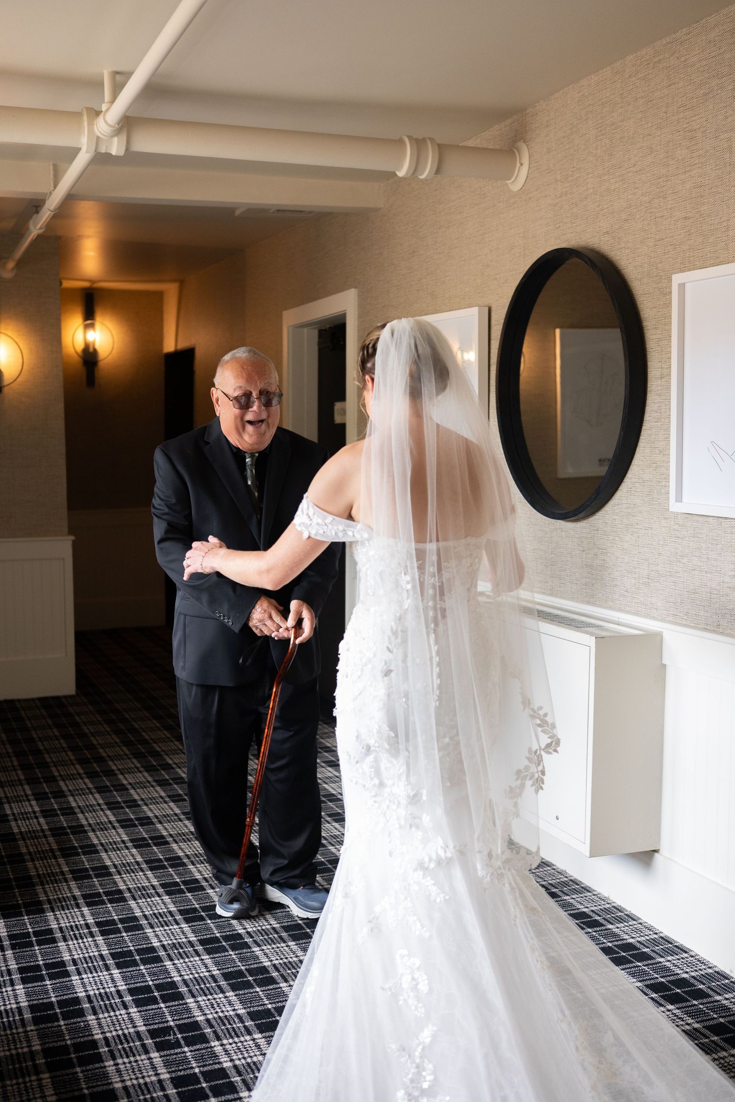 Emotional father reacts with joy seeing bride in wedding dress and veil during first look moment.