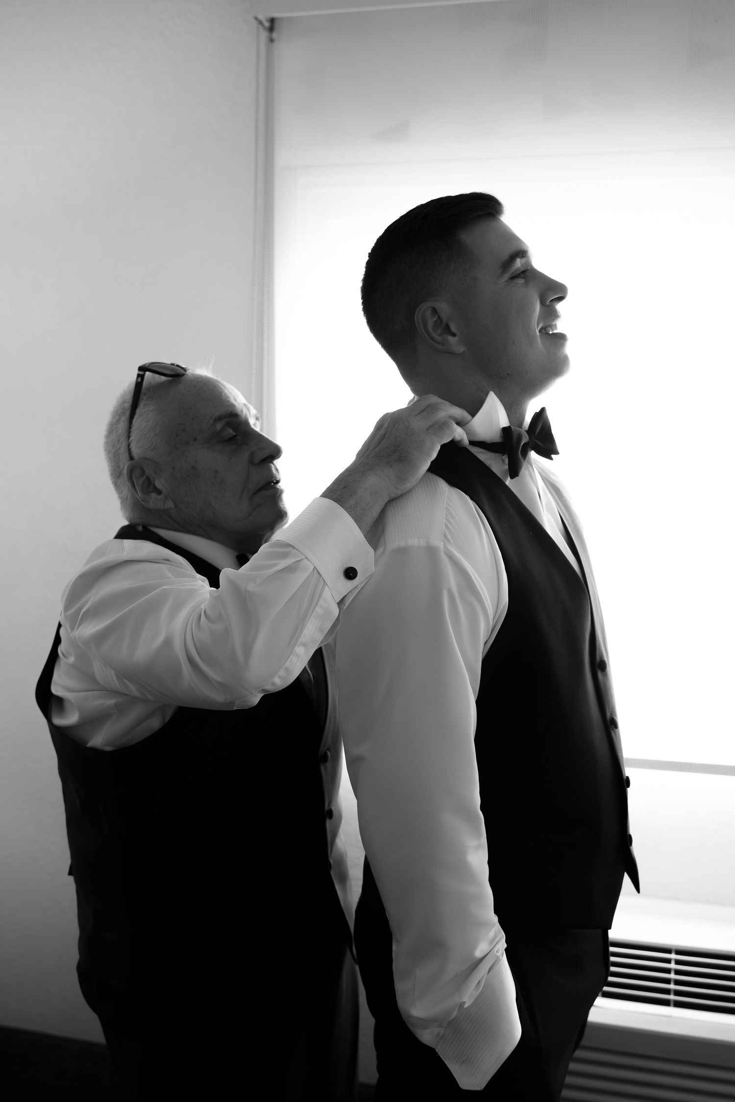 Father adjusting groom's bow tie before the wedding ceremony in a black and white portrait.