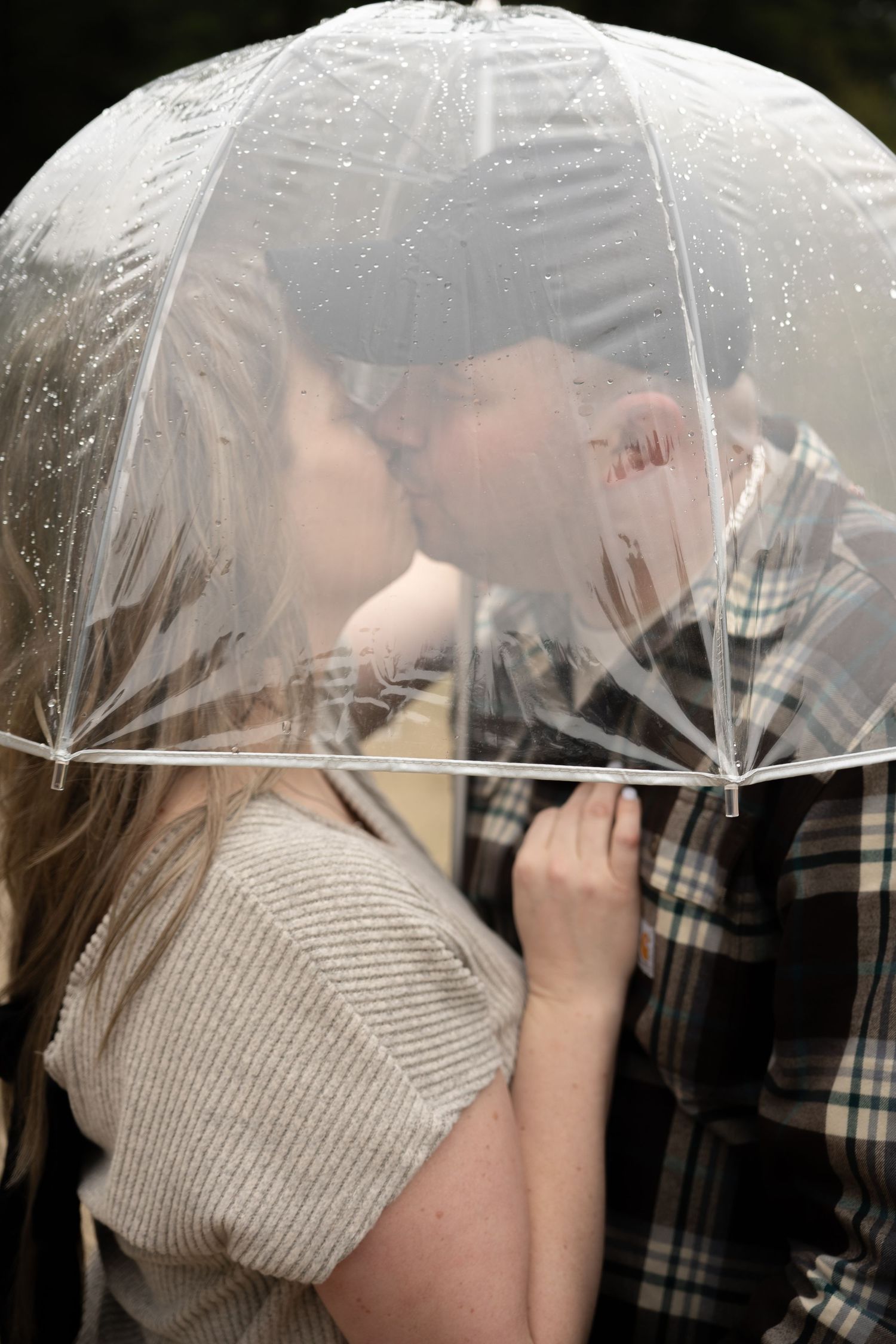 A couple shares a kiss under a clear bubble umbrella in the rain.