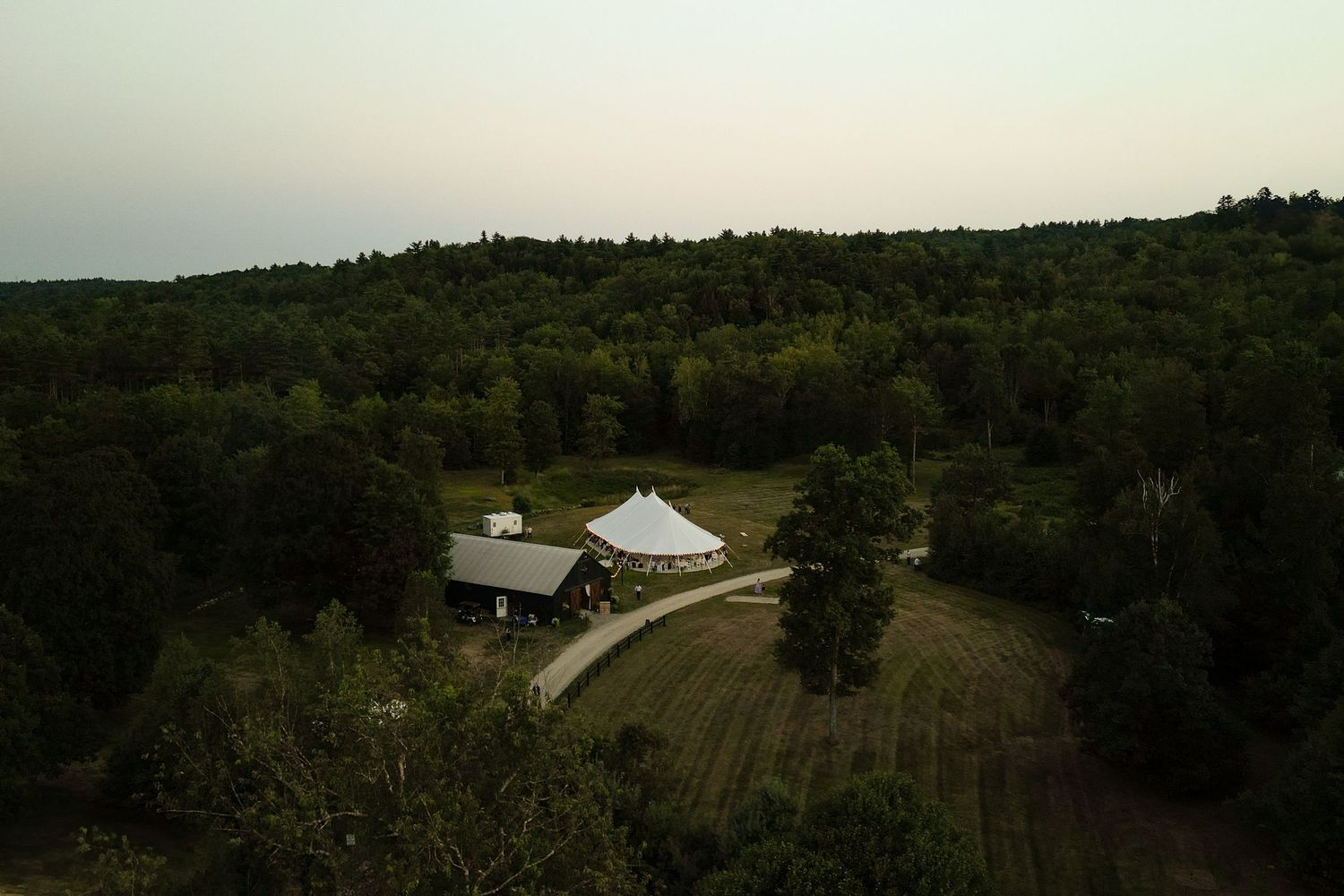 Aerial drone view of a wedding venue tent surrounded by dense forest at dusk.