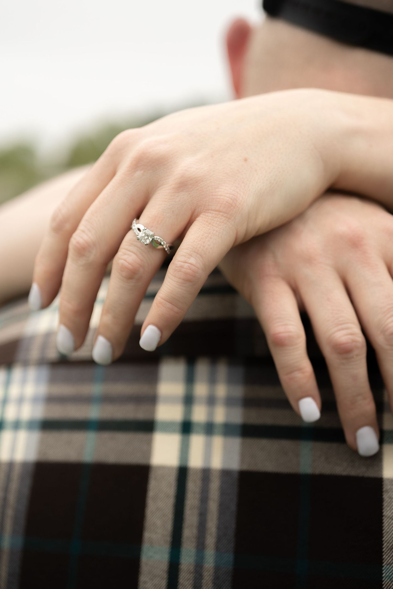 A woman displays her engagement ring while embracing a man in plaid.