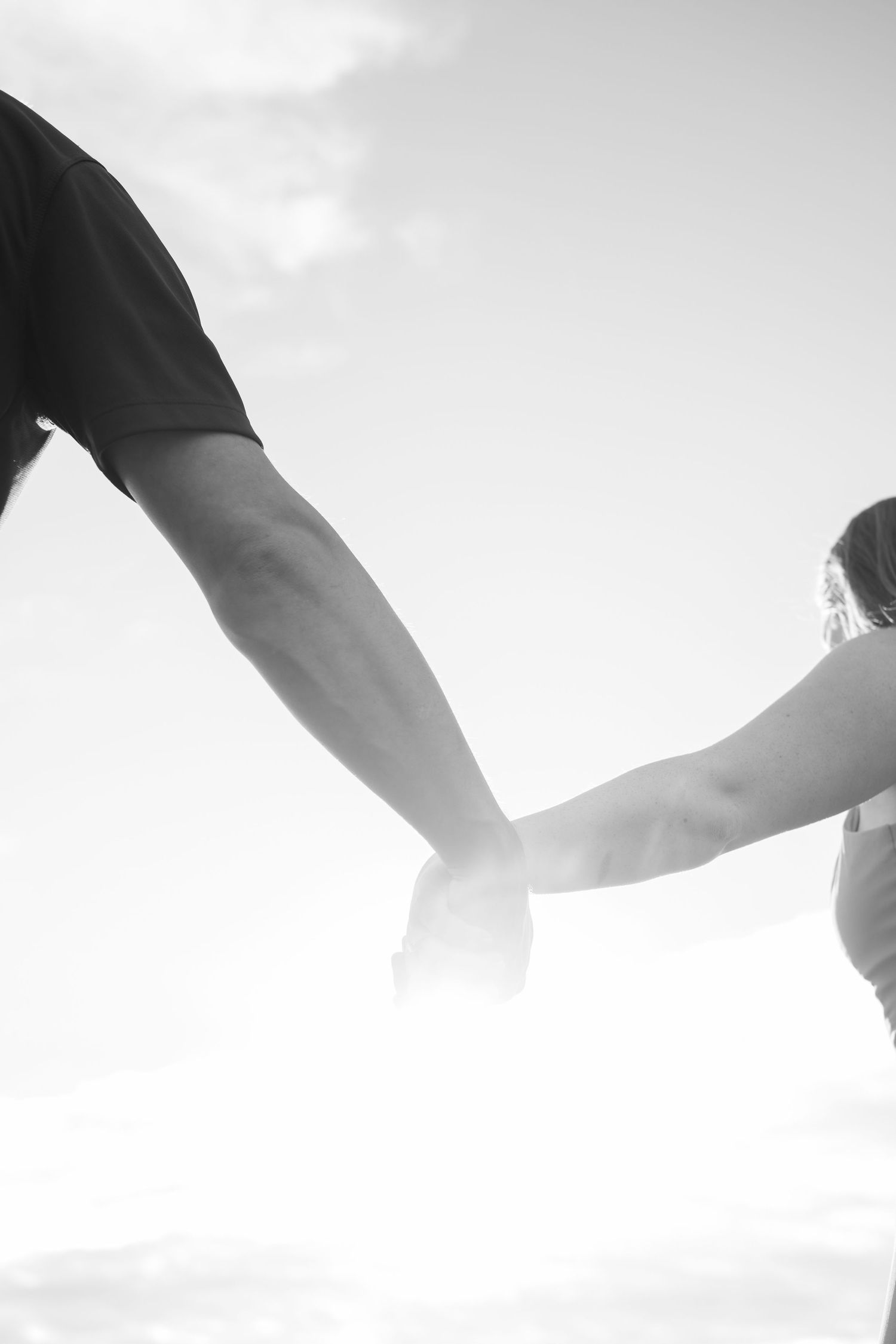 A black and white photo of a couple holding hands against the sky.