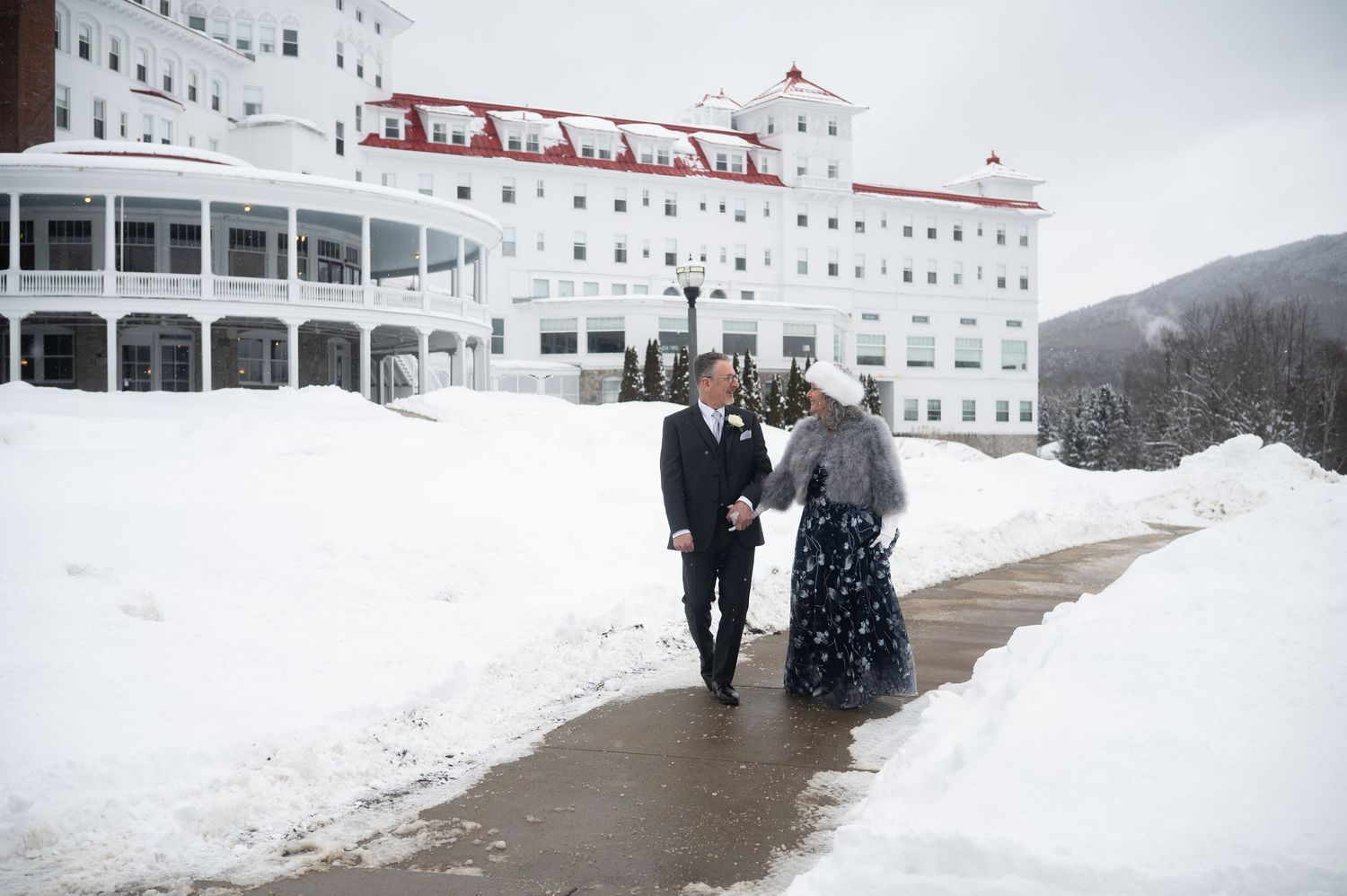 Wedding couple walking hand in hand outside a grand white hotel in deep winter snow.