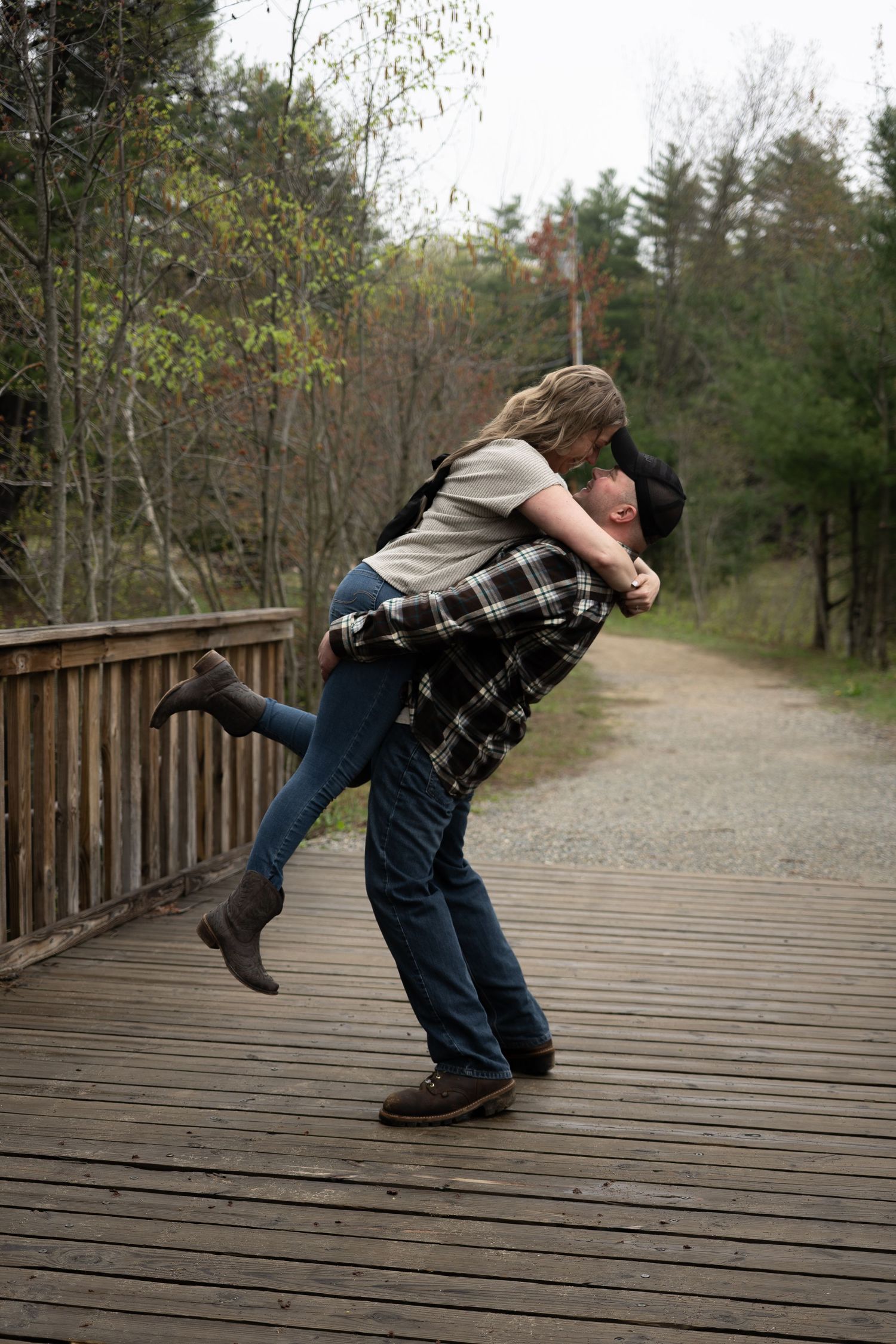 A man lifts a woman on a wooden bridge surrounded by autumn trees.