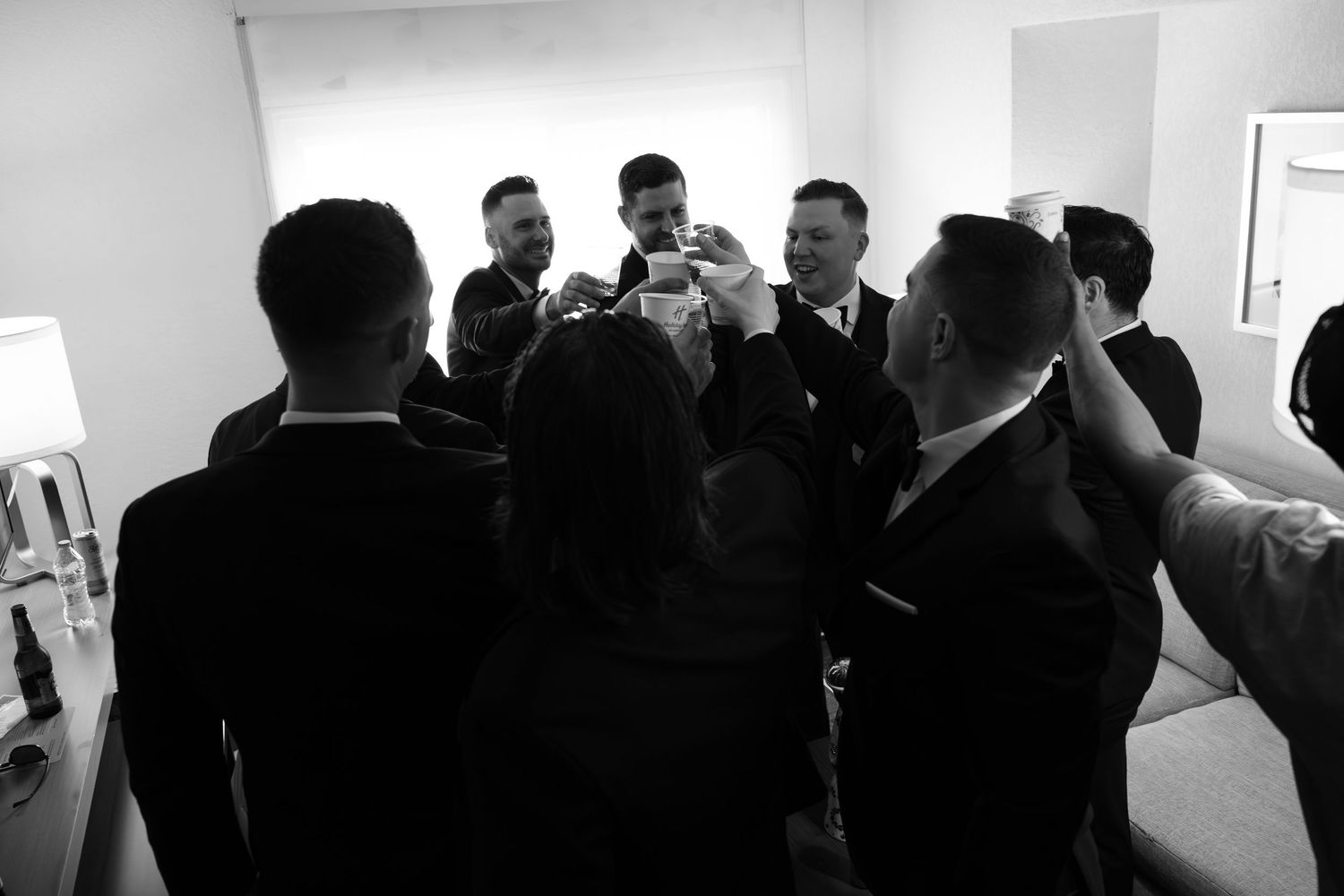 Groomsmen gathered in a circle raising glasses for a toast in a black and white wedding photo.
