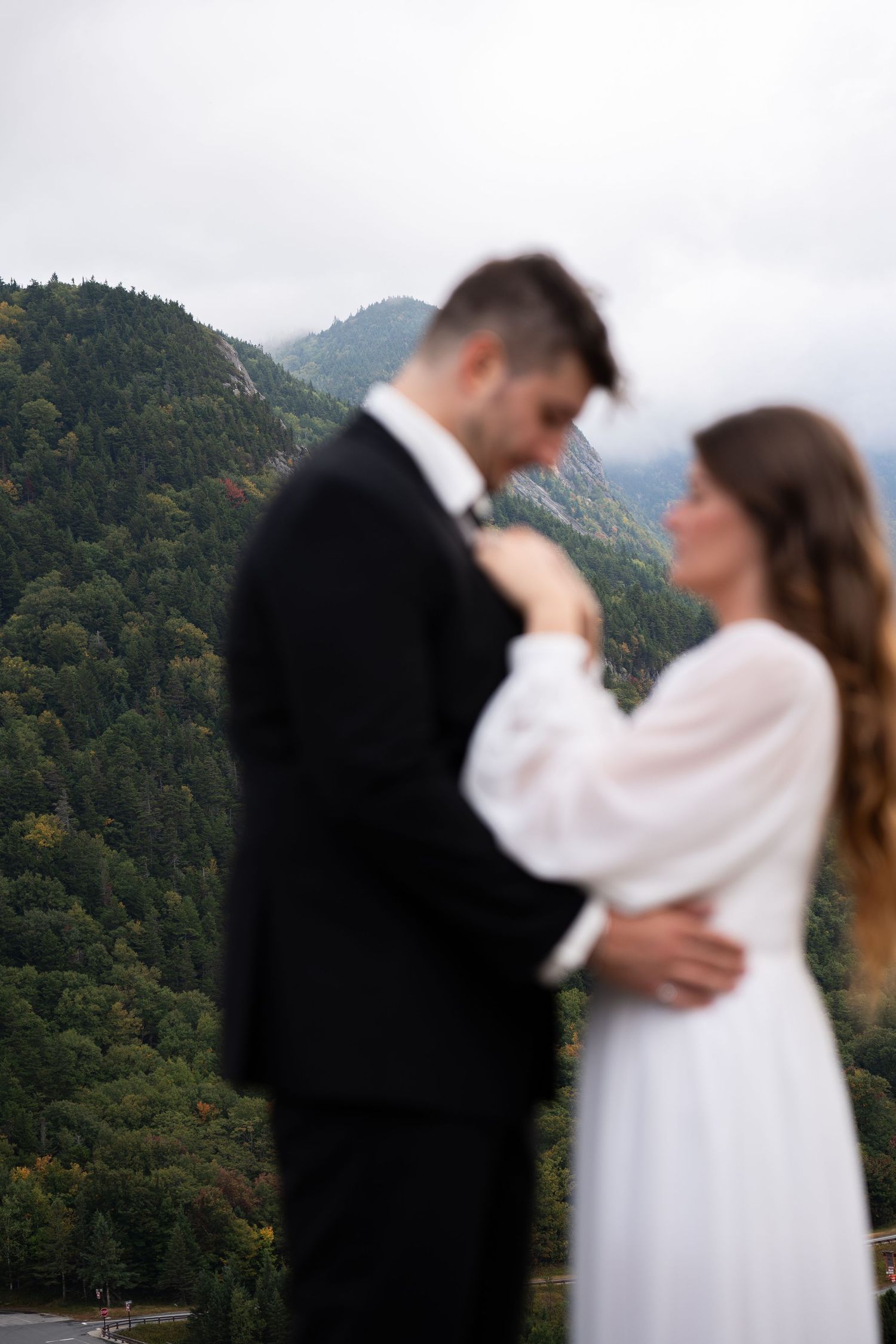 Bride and groom embracing with misty mountain forest backdrop on their wedding day.