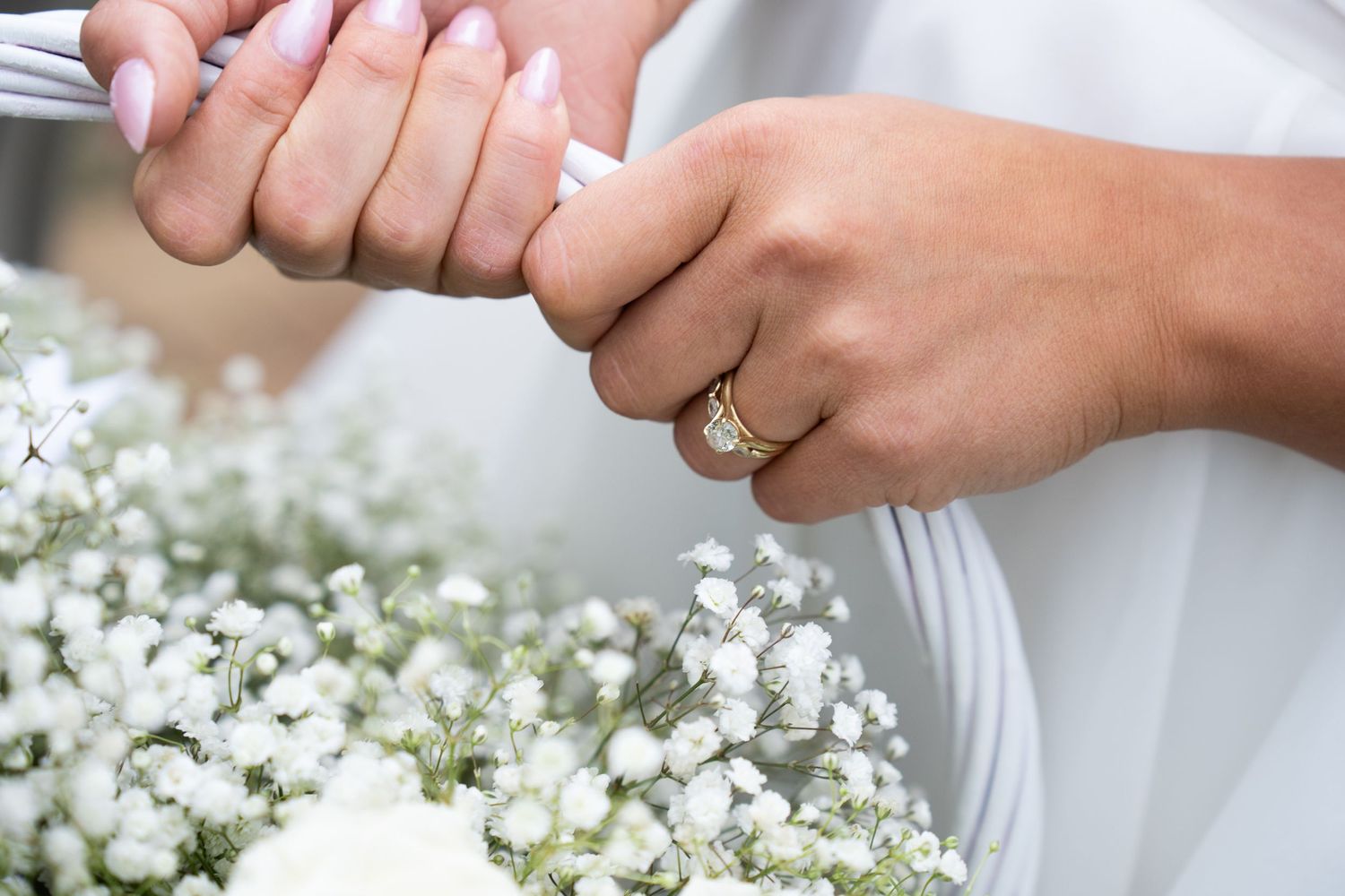 Close-up of bride and groom holding hands with diamond engagement ring and wedding bouquet of baby's breath.