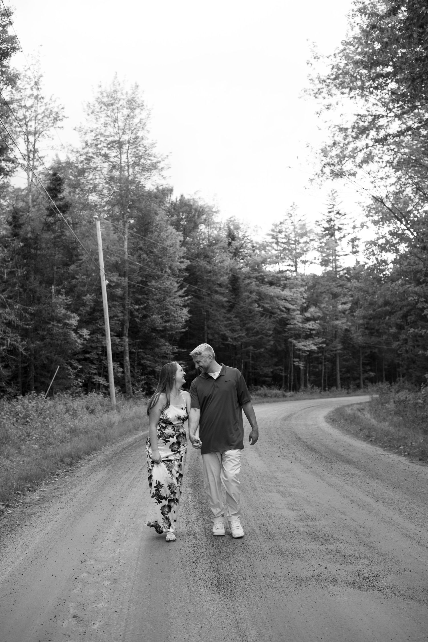 Black and white photo of couple walking together on a winding forest dirt road.