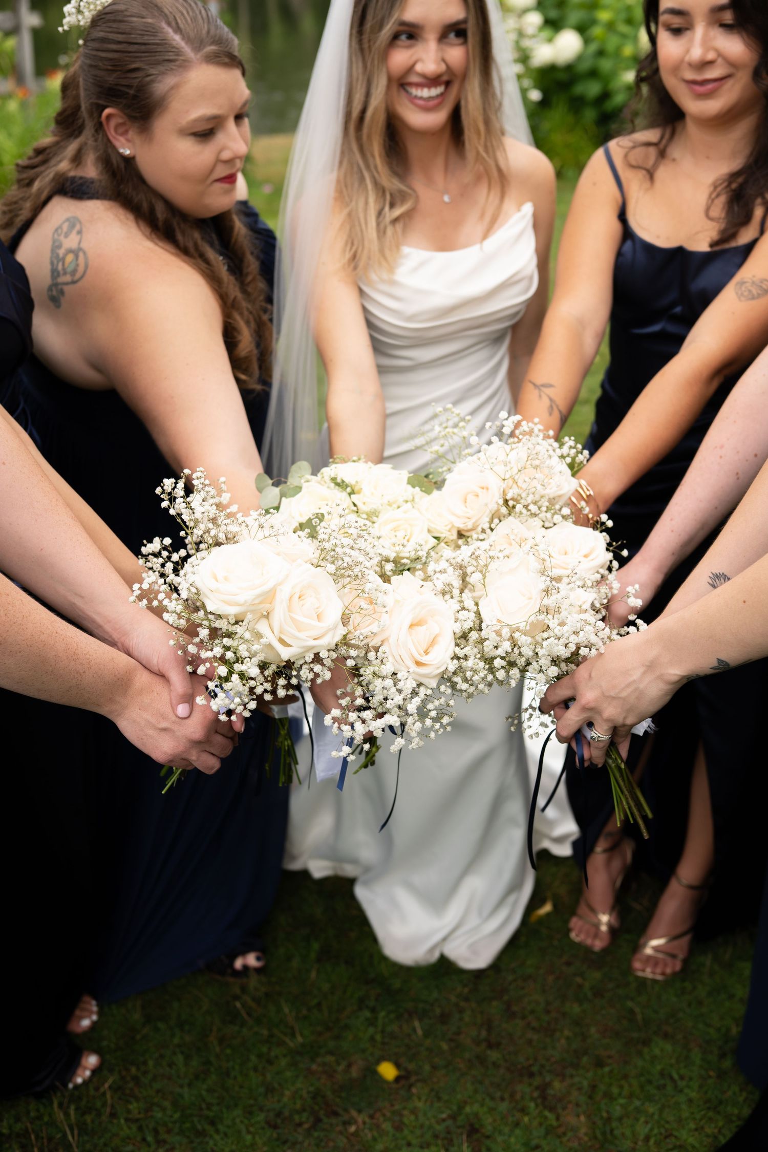 Bride and bridesmaids in navy dresses holding white rose and baby's breath bouquet.