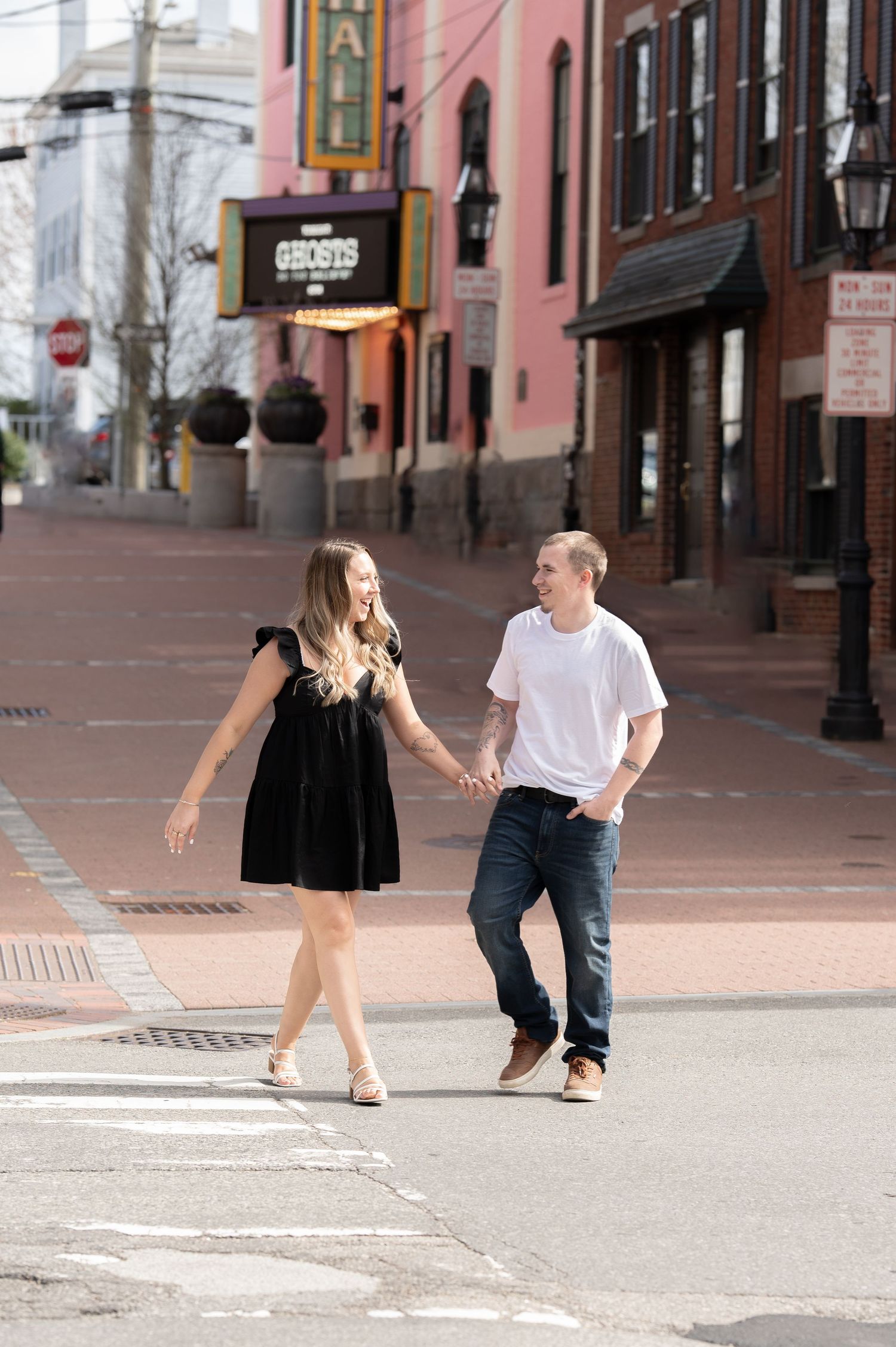 Couple holds hands and laughs while crossing a downtown street past a historic theater marquee.