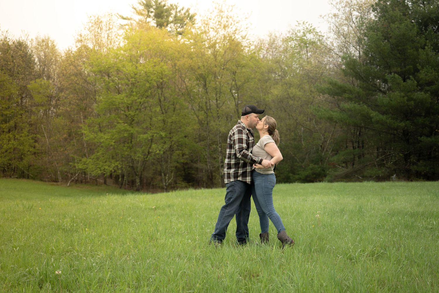 A couple embraces and kisses in a lush green field at sunset.