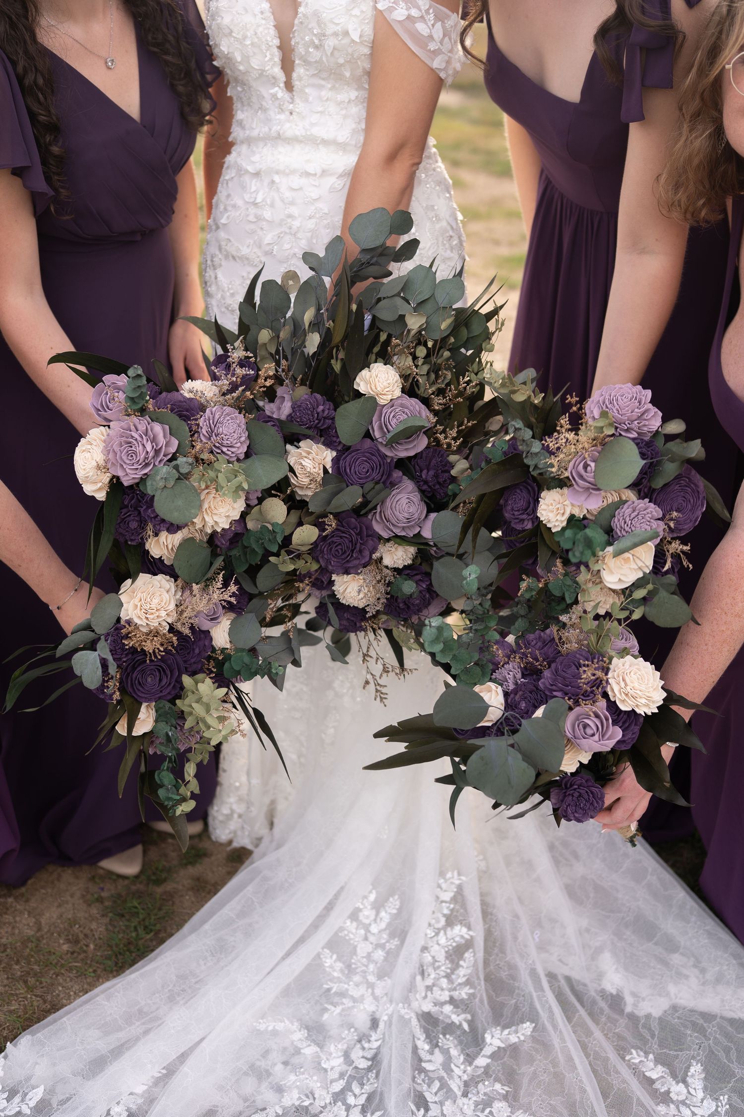 Bride and bridesmaids in purple dresses holding lush bouquets of lavender, cream, and deep purple flowers with eucalyptus.
