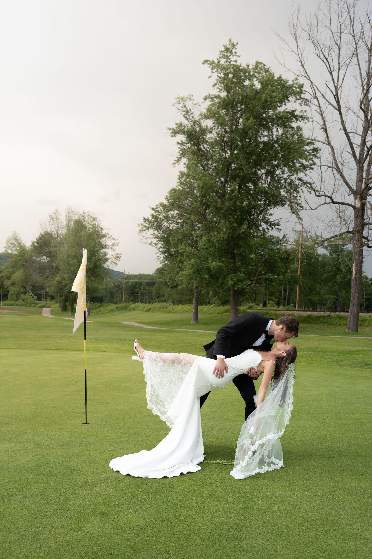 Bride and groom sharing a romantic dip kiss on a lush green golf course with a flag pin nearby.