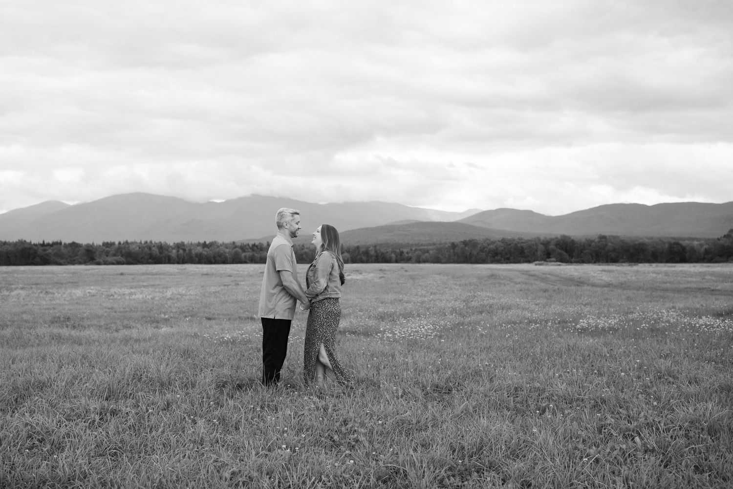 A black and white photo of a couple standing in a field with mountains.